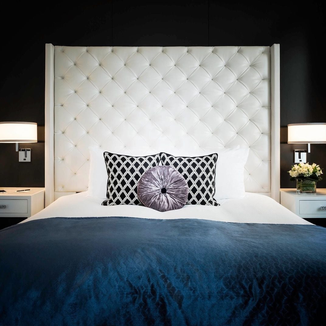 Tufted ivory leather headboards and crisp navy velvet create sophisticated contrast in guest rooms, where geometric pillows add modern edge to classic luxury.