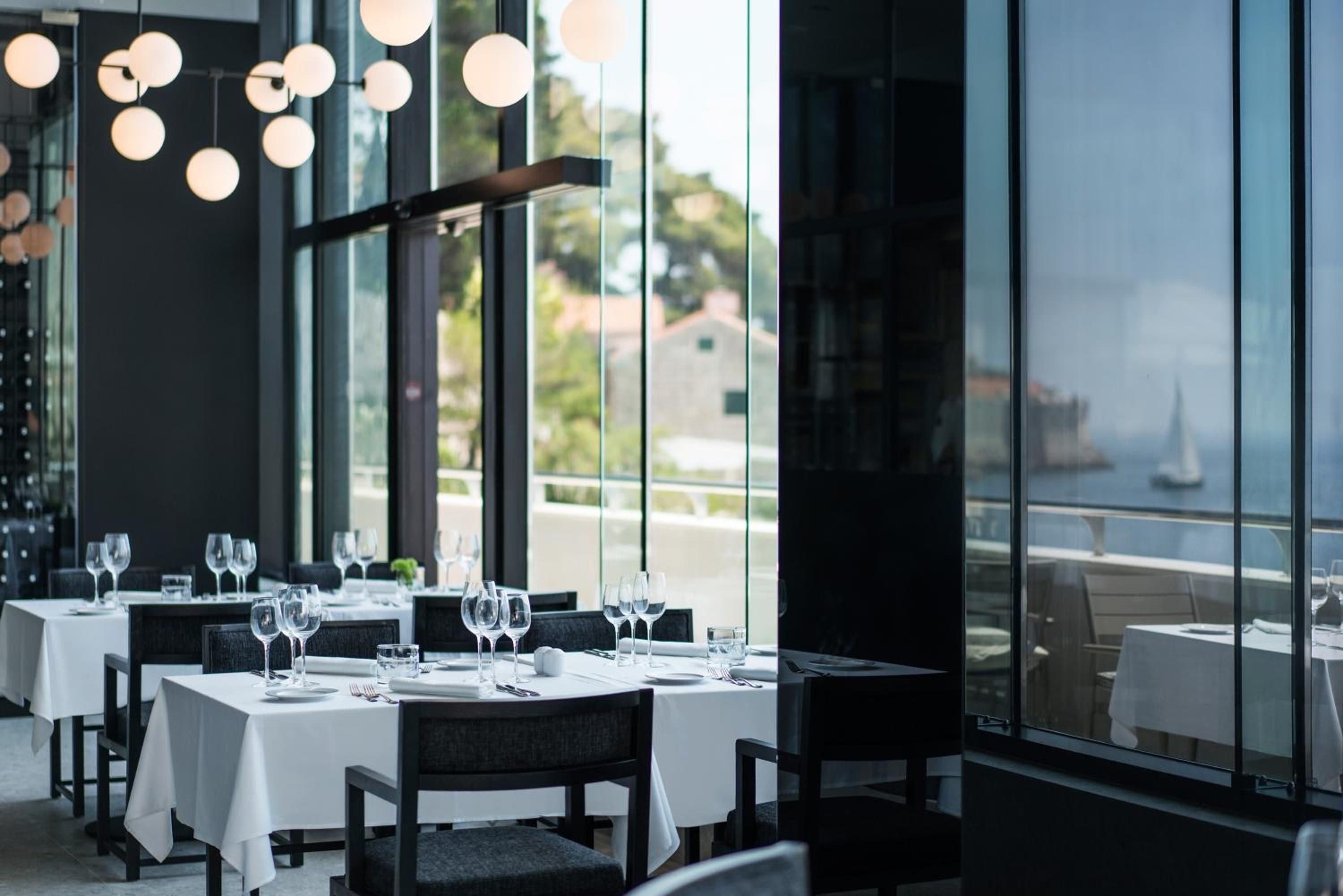 Floor-to-ceiling windows frame verdant hillsides while sculptural pendant lights cast a warm glow over crisp linens and precisely arranged stemware in the hotel's signature dining room.