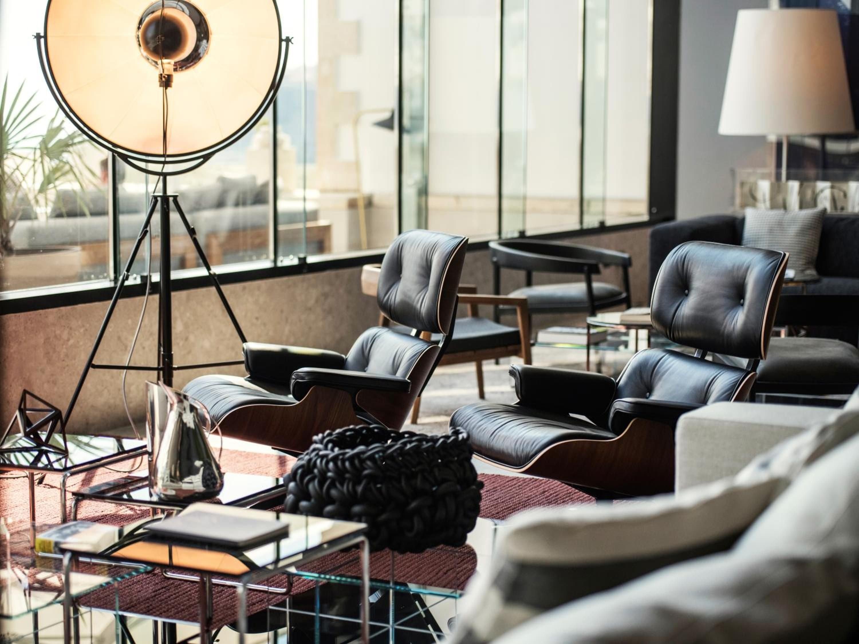 Mid-century leather loungers and industrial tripod lighting create an effortlessly sophisticated gathering space where natural light streams through floor-to-ceiling windows.
