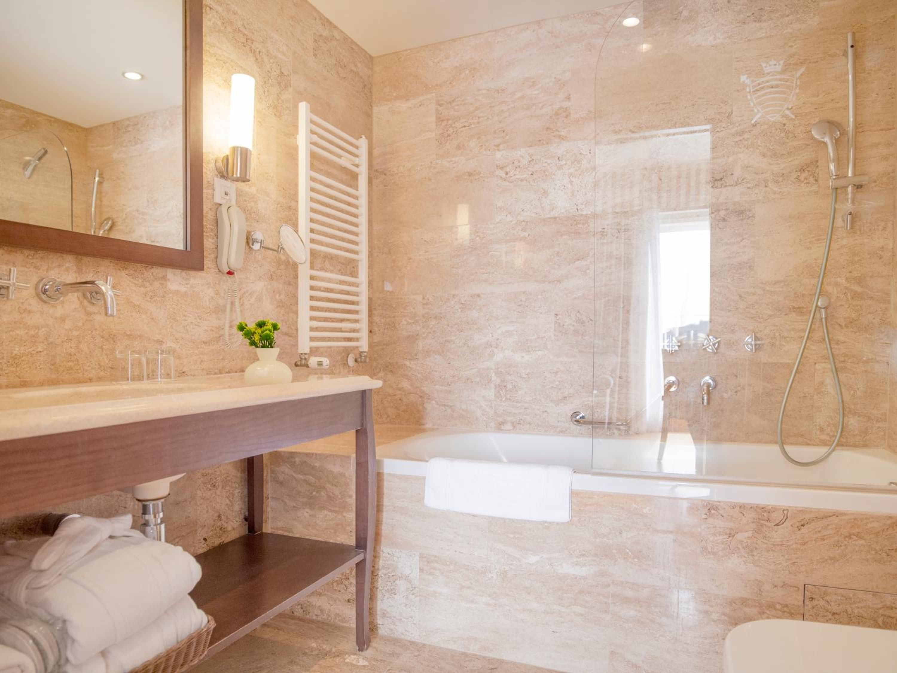Warm travertine wraps this spa-like sanctuary where heated towel rails and rain showers create a luxurious retreat bathed in honey-toned stone.
