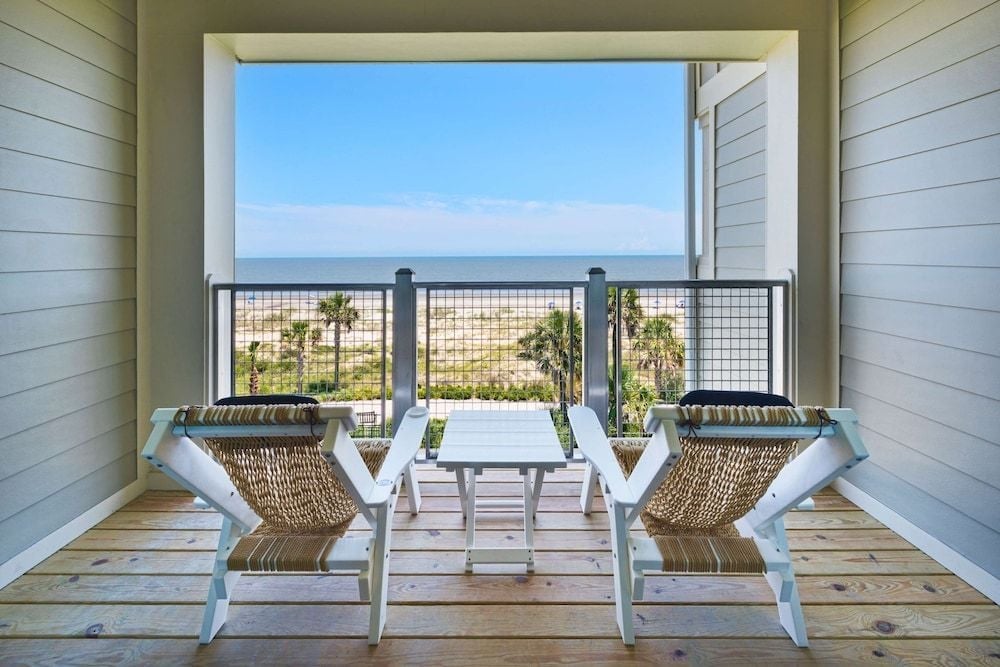 Woven rope chairs frame an ocean vista from this private balcony, where salt air mingles with the rustle of palm fronds below.