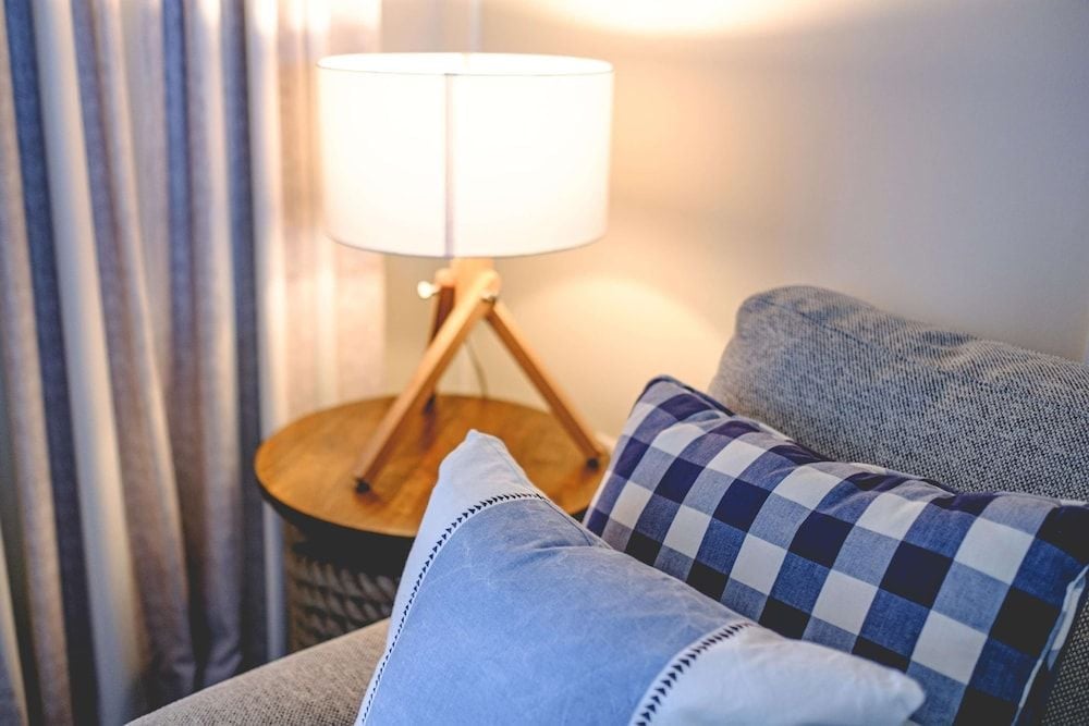 Soft lamplight illuminates thoughtfully curated linens and gingham pillows, creating an intimate reading nook where coastal comfort meets refined simplicity.