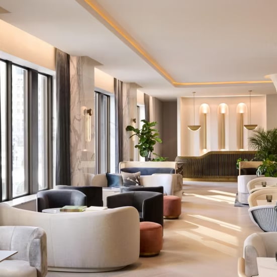 Curved seating clusters and warm marble columns create intimate conversation nooks beneath glowing cove lighting, while lush greenery softens the contemporary elegance of this welcoming reception space.