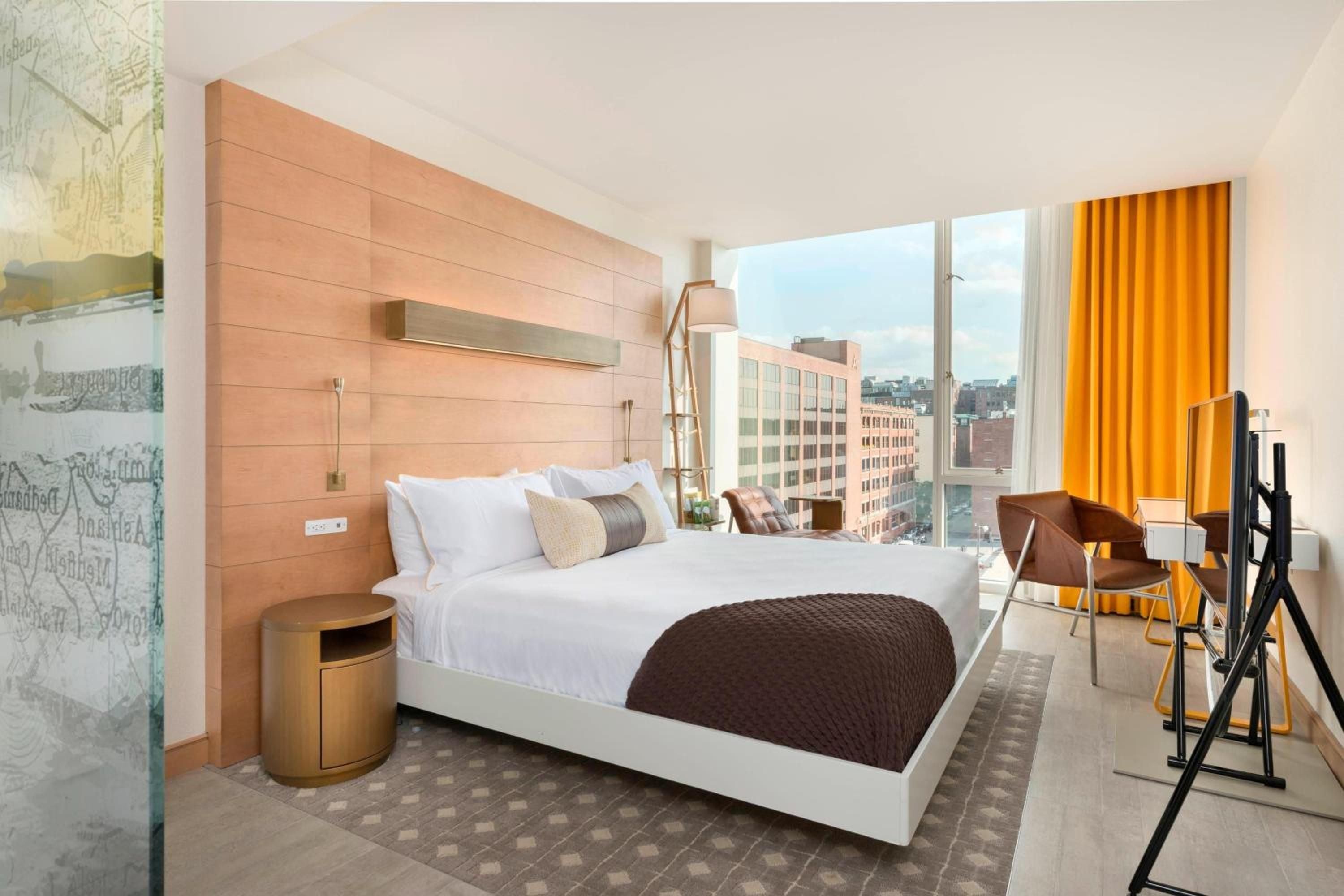 Floor-to-ceiling windows frame Boston's skyline while warm wood paneling and golden curtains create an inviting cocoon high above the bustling Seaport District.