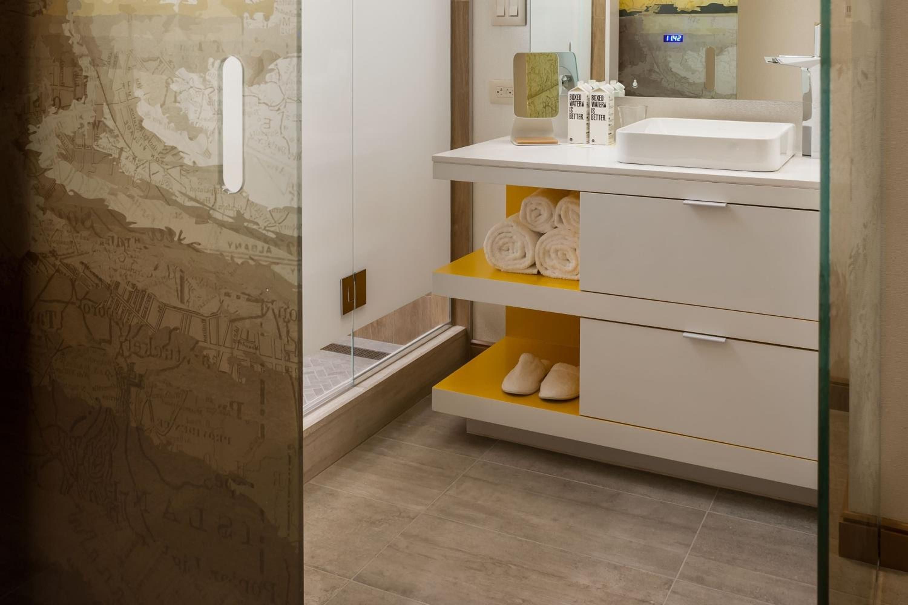 Floating vanity storage reveals thoughtful design touches, with golden accents brightening crisp white cabinetry while rolled towels and slippers await guests in clever cubbies.