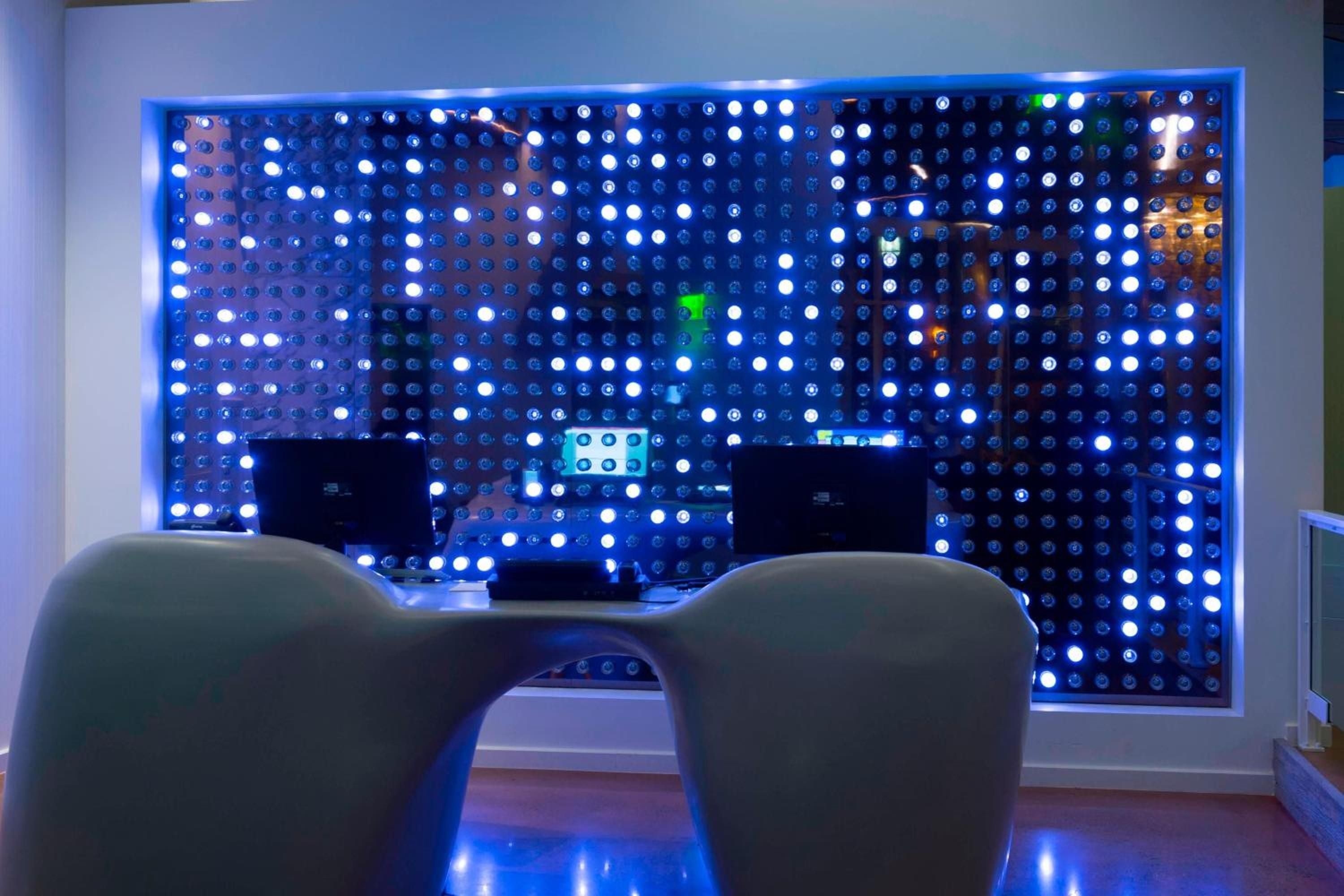 Futuristic pod chairs face an illuminated LED wall installation, creating an otherworldly lounge atmosphere where guests gather beneath the mesmerizing dance of blue and white lights.