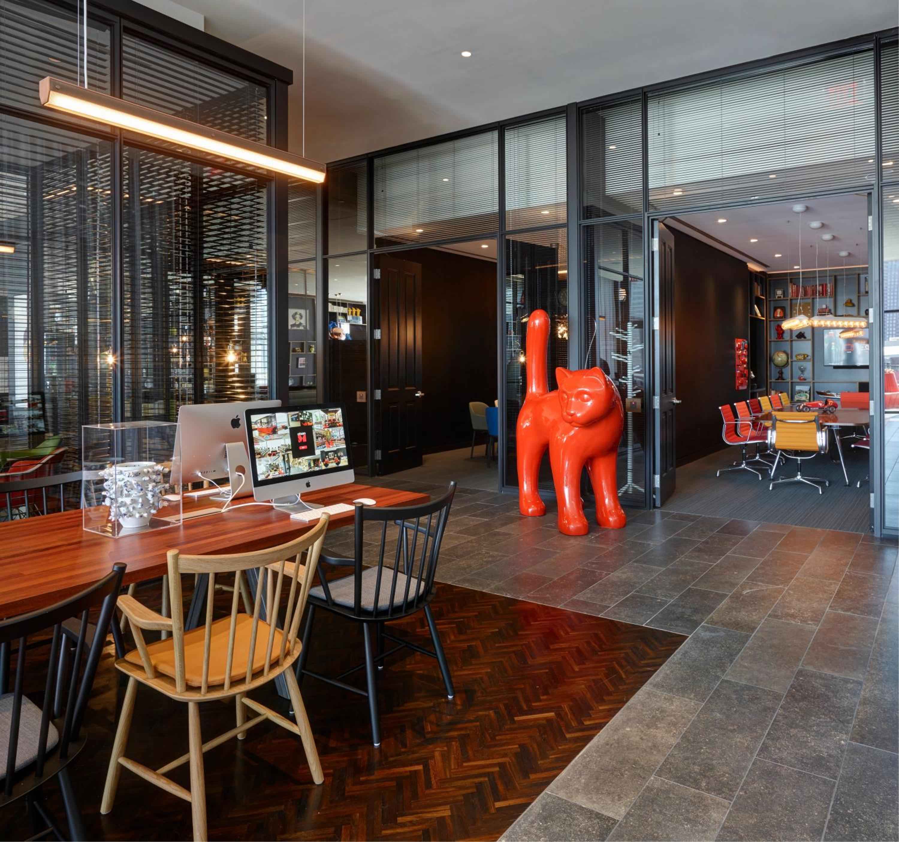 Warm wood parquet meets cool stone tiles while a whimsical red dog sculpture presides over citizenM's tech-forward lobby workspace, where business travelers gather beneath sleek pendant lighting.