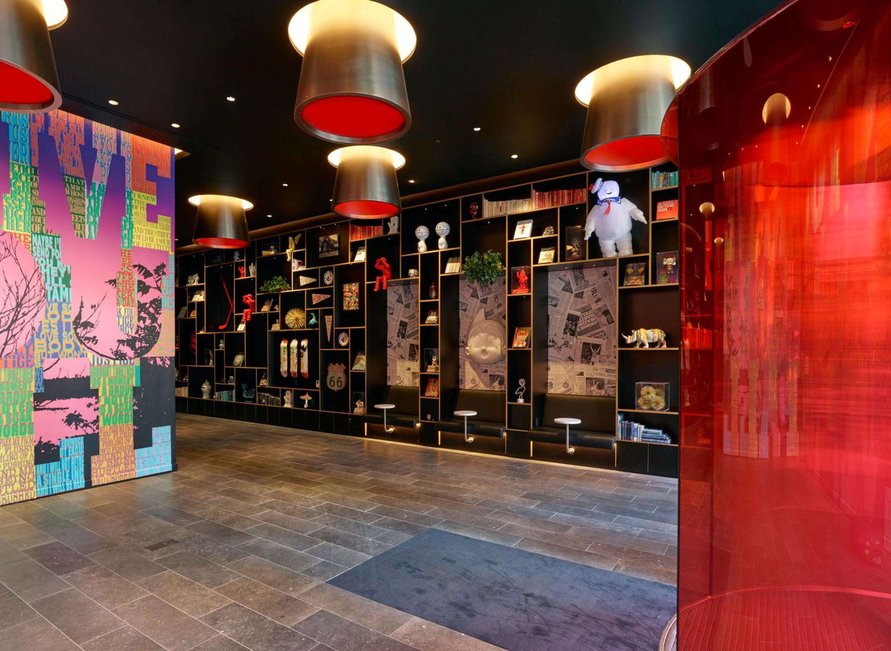 Cylindrical pendant lights cast warm glows over floor-to-ceiling shelving filled with curiosities, while vibrant street art creates an energetic backdrop in the communal space.