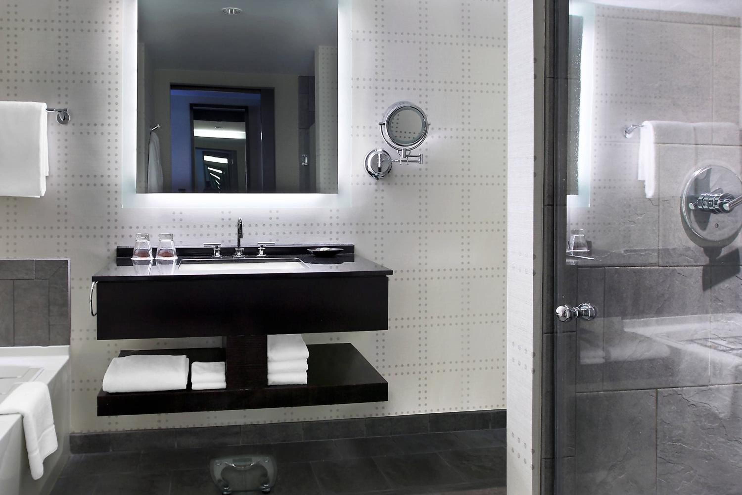 Sleek black granite vanities float against dotted white walls, while polished chrome fixtures catch light from the illuminated mirror in this sophisticated guest bathroom.