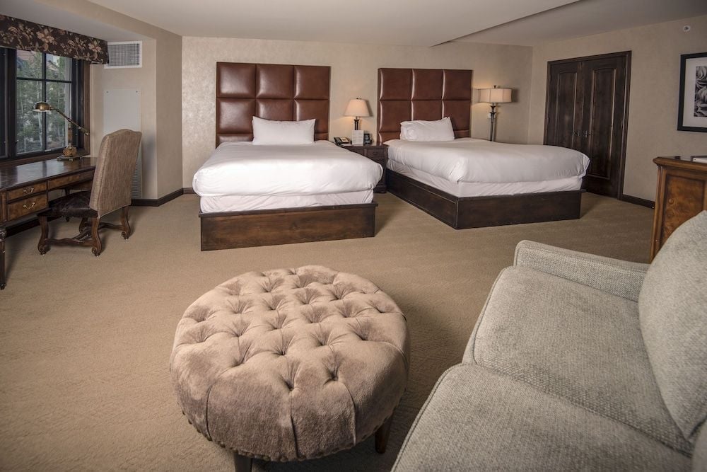 Tufted leather headboards and rich walnut frames anchor this spacious double-queen suite, where neutral linens and mountain lodge textures create refined alpine comfort.