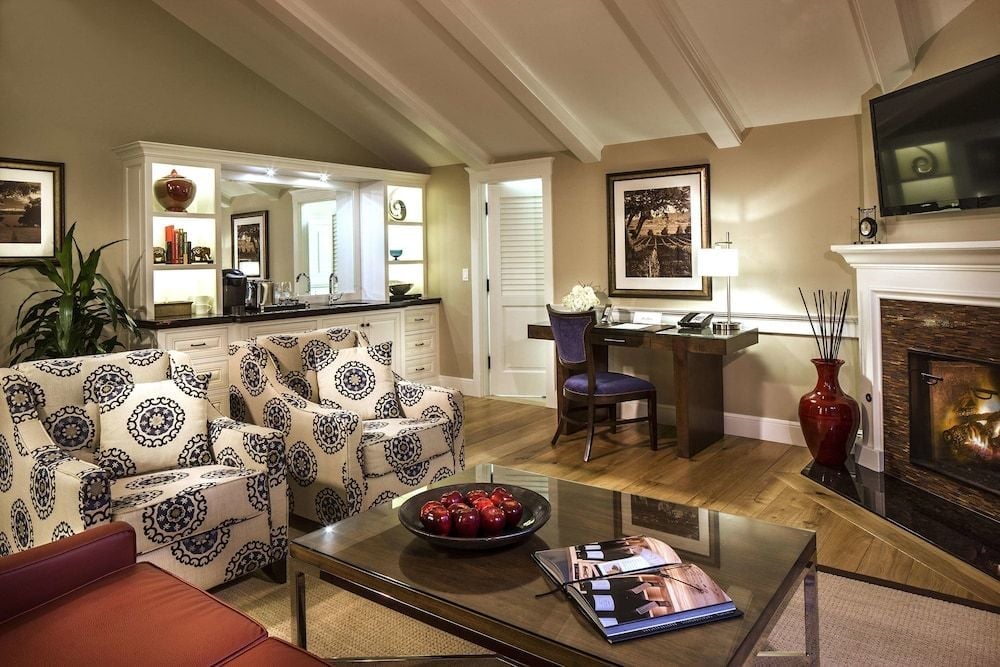 Exposed ceiling beams frame a sophisticated living area where patterned armchairs gather around a sleek coffee table, while a workspace and fireplace create intimate zones.