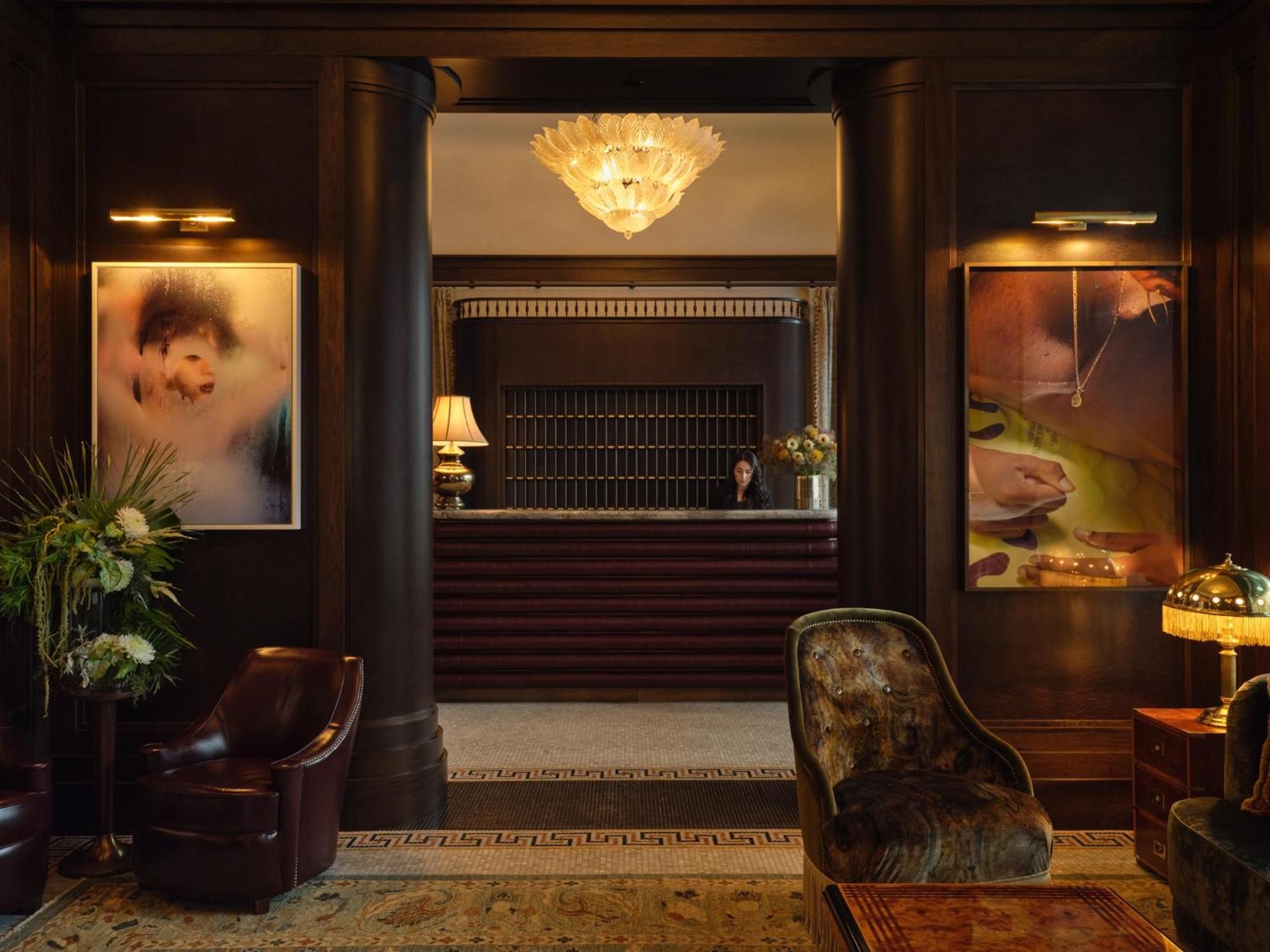 Rich mahogany paneling and oversized art create an intimate receiving area where golden light from crystal chandeliers bathes velvet armchairs in warmth.