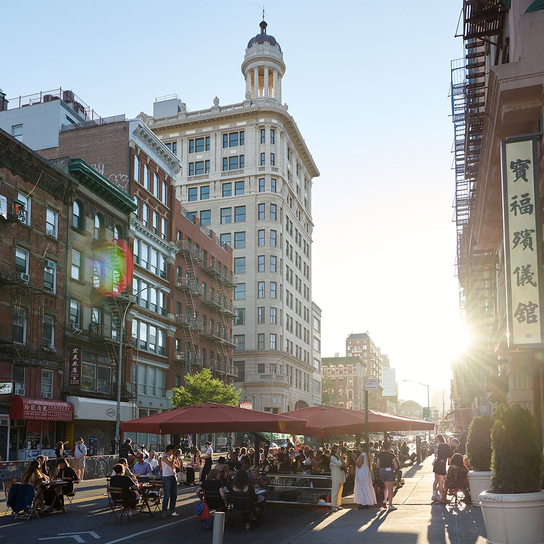 Golden hour light bathes the historic Beaux-Arts tower and bustling street scene below, where outdoor dining spills onto sidewalks amid Chinatown's vibrant energy.