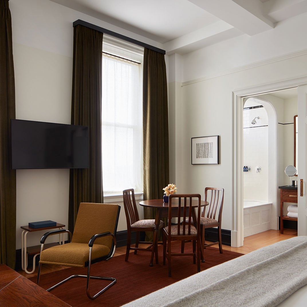 Warm wood floors and chocolate velvet curtains create an intimate seating nook, where mid-century chairs gather around a petite dining table beside the modern fireplace.