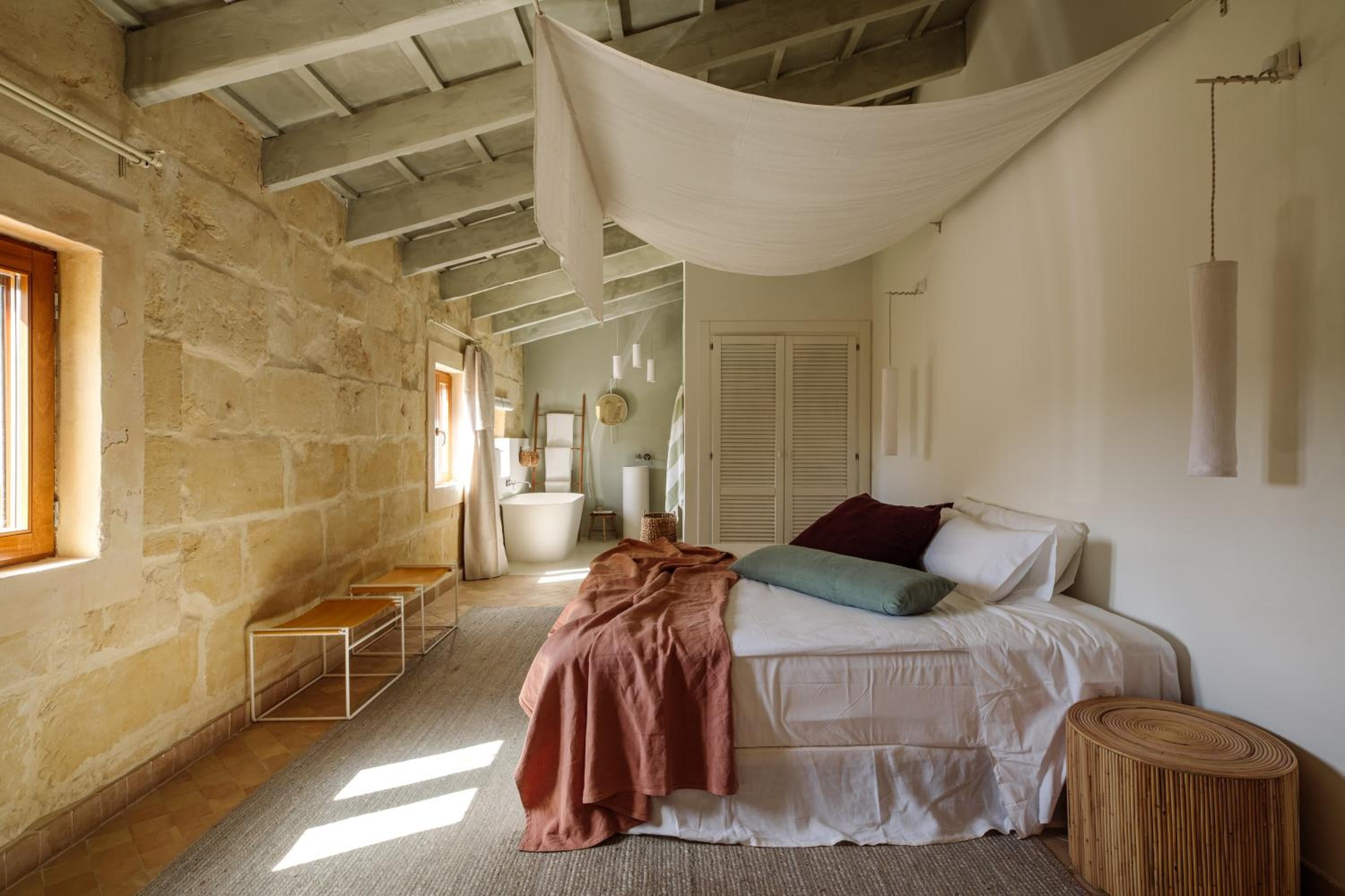 Natural stone walls and flowing white canopy create an intimate sanctuary, where rustic charm meets modern comfort in this thoughtfully appointed suite.