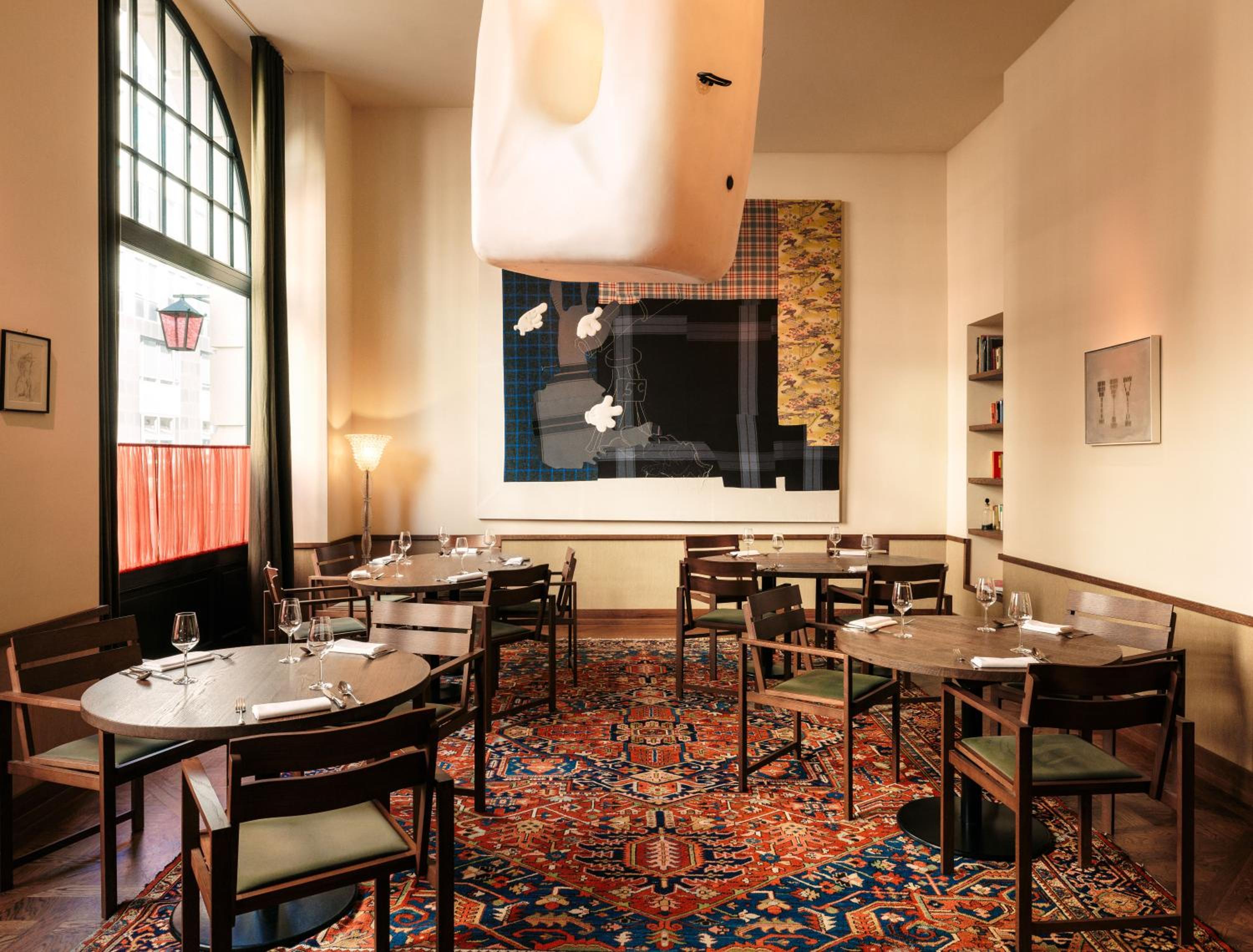 Warm afternoon light filters through industrial windows onto Persian rugs and contemporary art, creating an intimate dining atmosphere where modern meets eclectic charm.