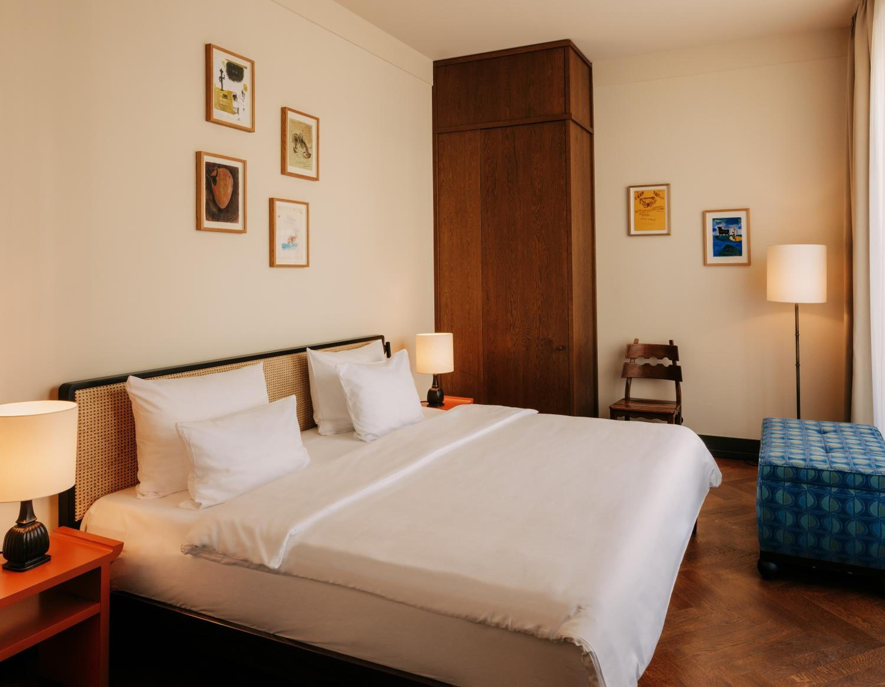 Warm wood tones and crisp white linens create a serene sanctuary, where curated artwork and thoughtful lighting invite quiet contemplation after exploring the château grounds.
