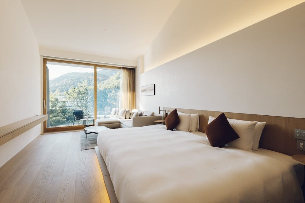 Floor-to-ceiling windows frame Kyoto's forested mountains while twin beds rest on warm wood platforms, creating a serene sanctuary where nature becomes art.
