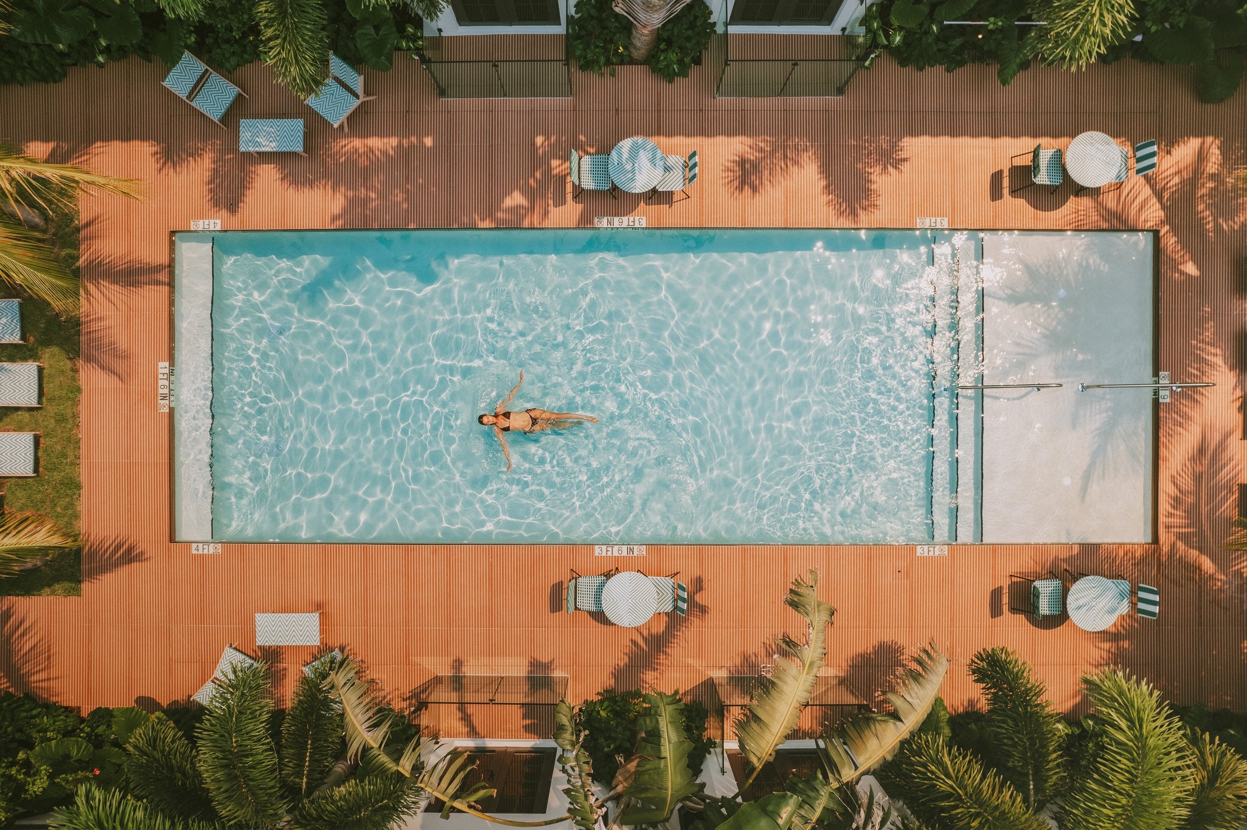 Palm shadows dance across terracotta tiles as a lone swimmer glides through crystal waters, the infinity pool's geometric perfection framed by tropical greenery.