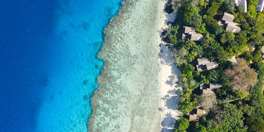 Coral reefs shimmer beneath crystal waters as intimate overwater bungalows nestle among emerald palms, creating Fiji's most secluded romantic sanctuary.