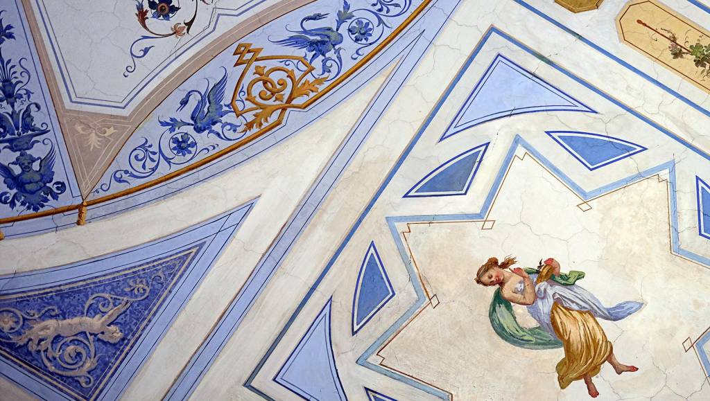 Hand-painted frescoes dance across vaulted ceilings, where azure geometric patterns frame delicate cherubs and golden flourishes in this exquisite display of Italian artistry.