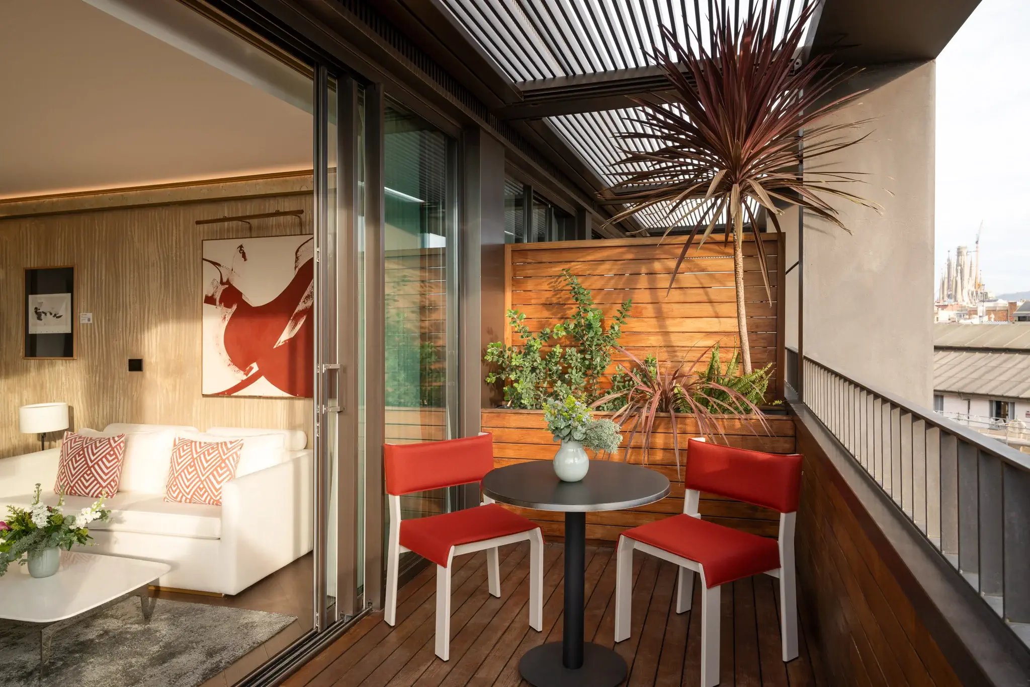 Warm wood decking and vibrant coral-red seating create an intimate terrace retreat, where Mediterranean light filters through slatted screens above Barcelona's rooftops.