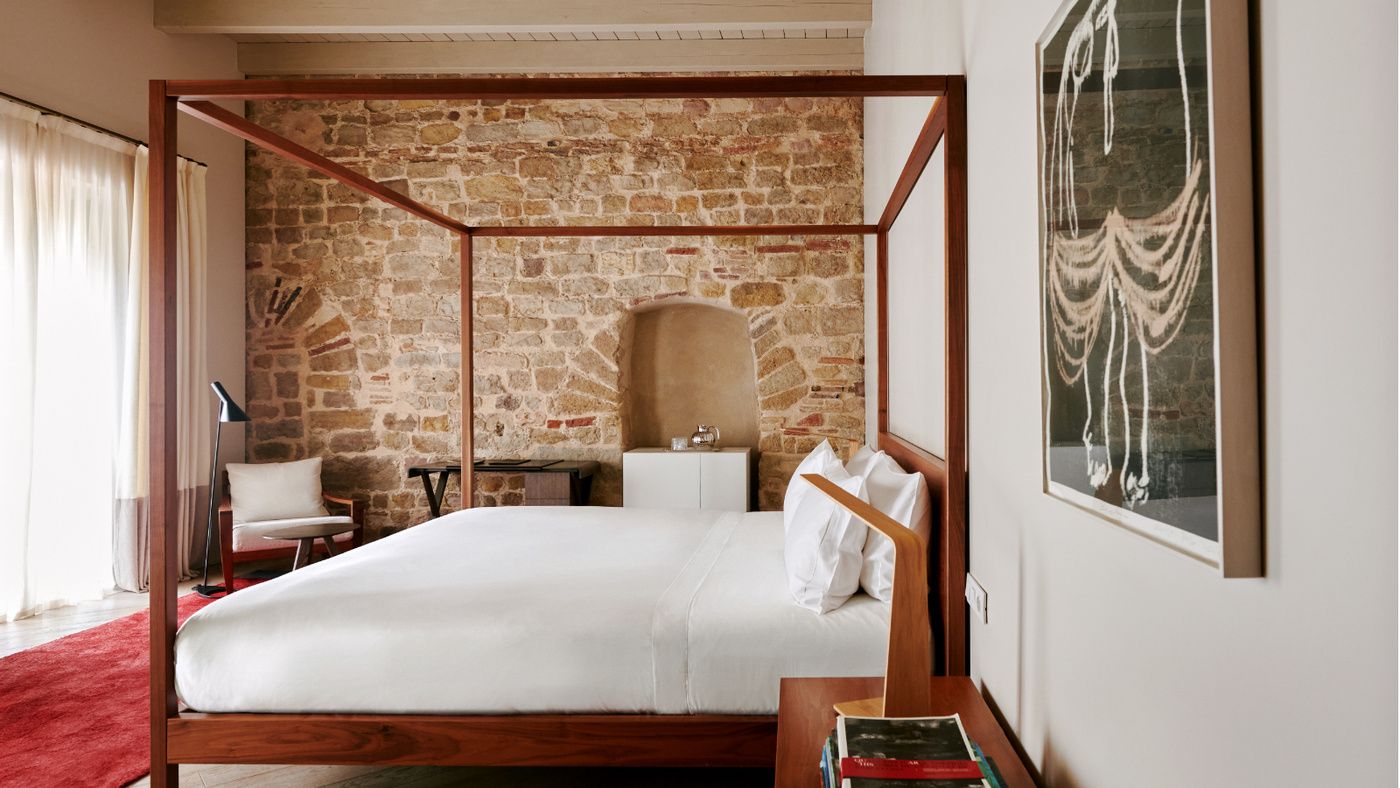 Exposed stone walls frame a walnut four-poster bed, where medieval Barcelona meets contemporary comfort beneath soaring beamed ceilings and crisp white linens.