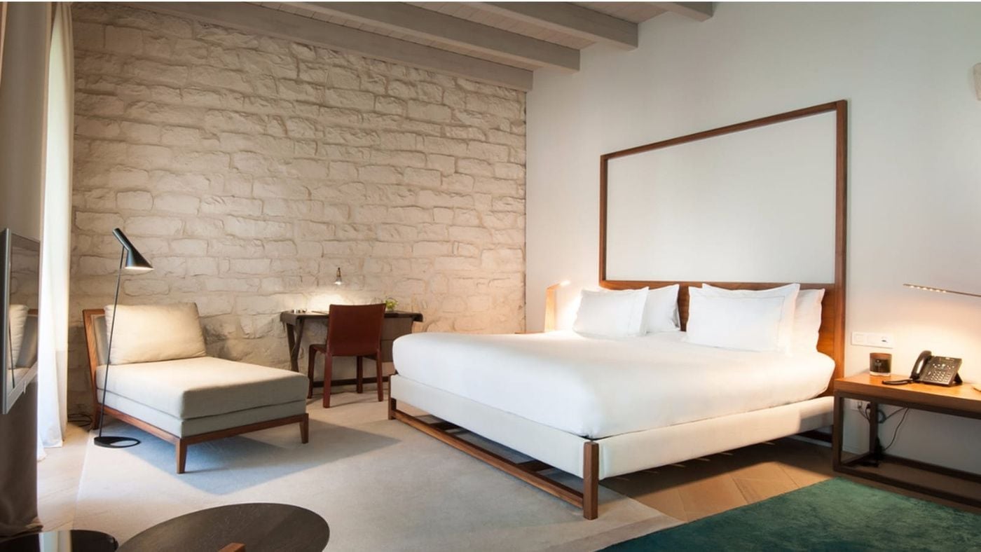 Exposed stone walls and warm wood furnishings create an intimate sanctuary where medieval Barcelona meets modern comfort in this thoughtfully designed guest room.