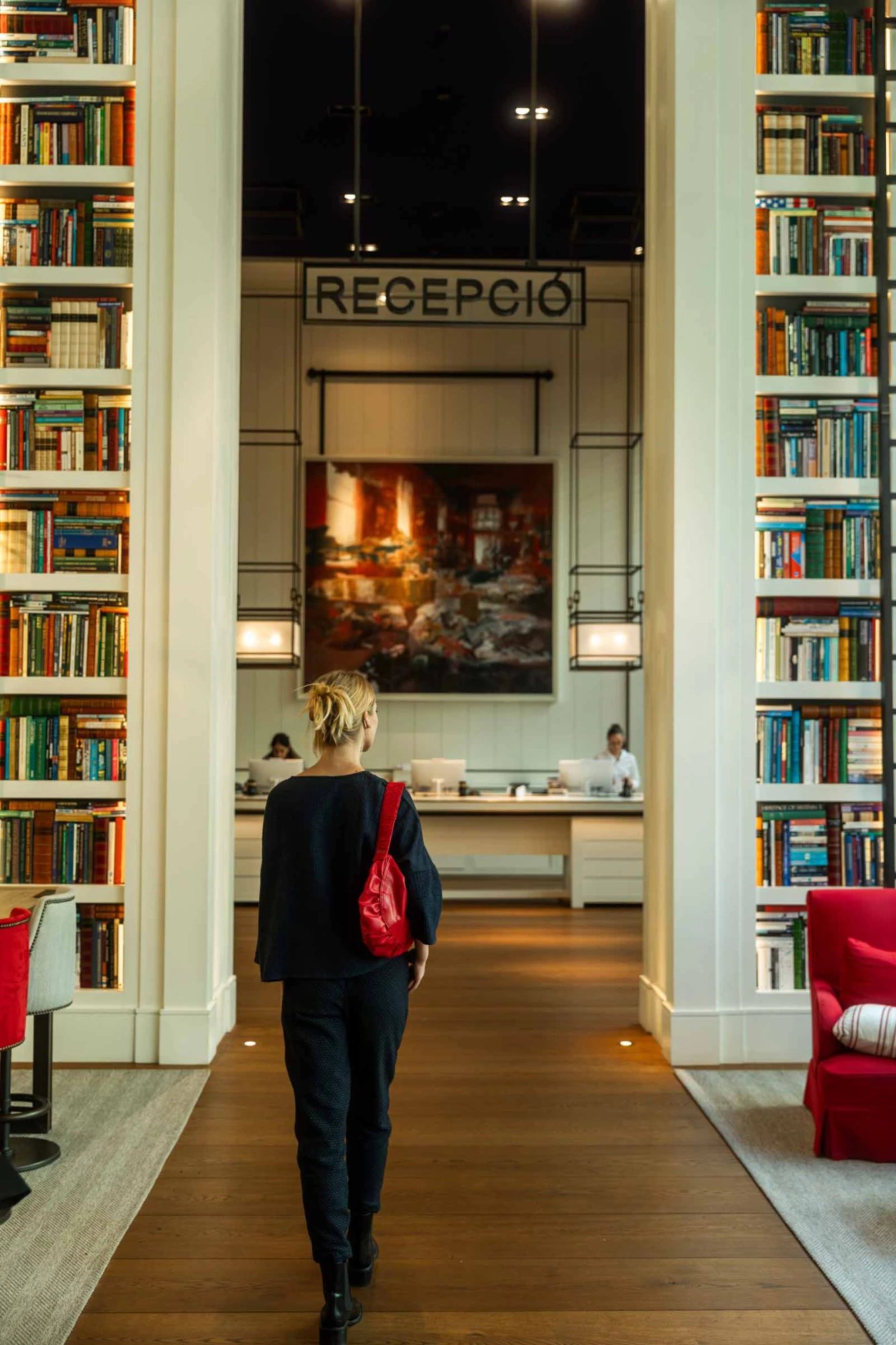 Floor-to-ceiling bookshelves frame the reception area, where warm wood floors and intimate lighting create a literary sanctuary in Barcelona's heart.