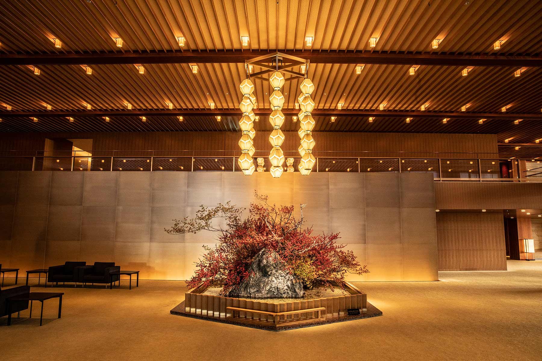 Geometric chandeliers cast honeyed light over the serene lobby, where a striking bonsai installation anchors the space beneath soaring timber-lined ceilings.