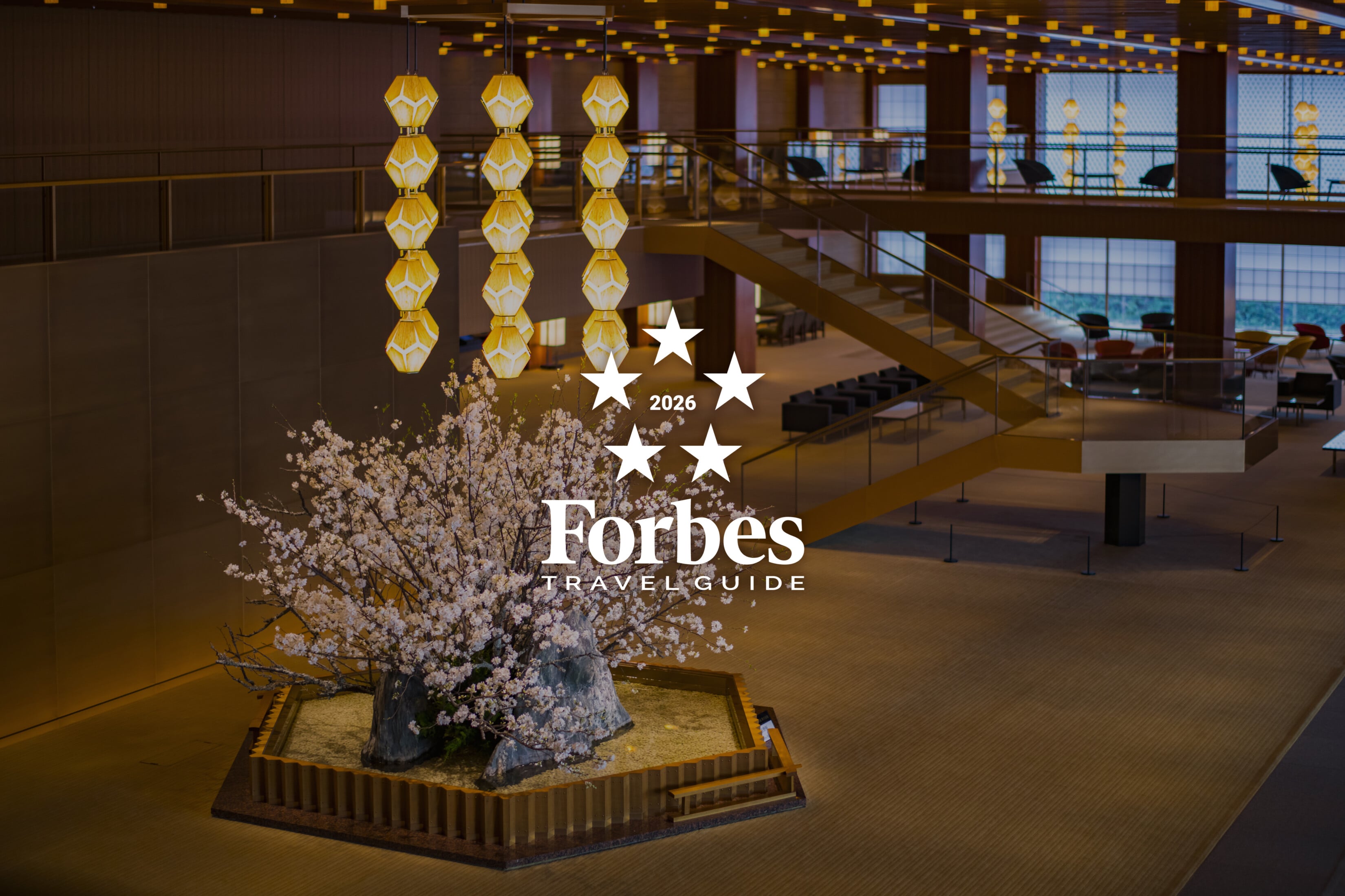 Golden pendant lights cast warm shadows across the serene lobby, where a sculptural cherry blossom installation bridges contemporary design with timeless Japanese artistry.