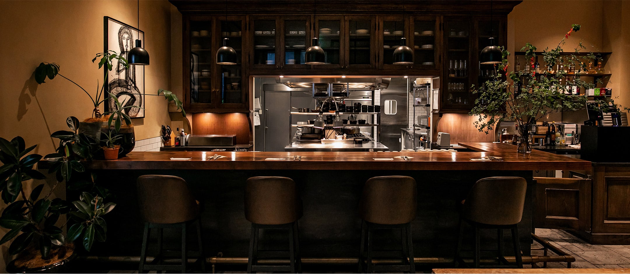 Copper-topped bar stools invite lingering conversations beneath pendant lighting, while the open kitchen's warm glow creates an intimate chef's counter experience perfect for solo dining.