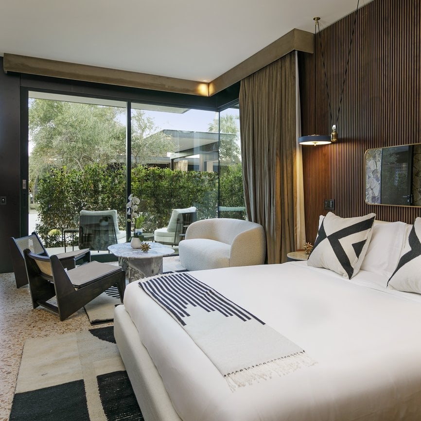 Floor-to-ceiling windows frame verdant gardens while warm wood paneling and crisp linens create an intimate sanctuary where modern luxury meets natural tranquility.