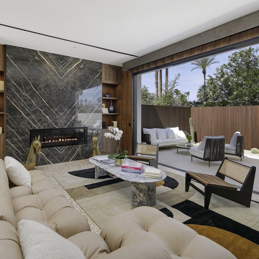 Warm wood paneling and dramatic marble chevron patterns frame this sophisticated living space, where natural light filters through floor-to-ceiling windows onto plush neutral furnishings.