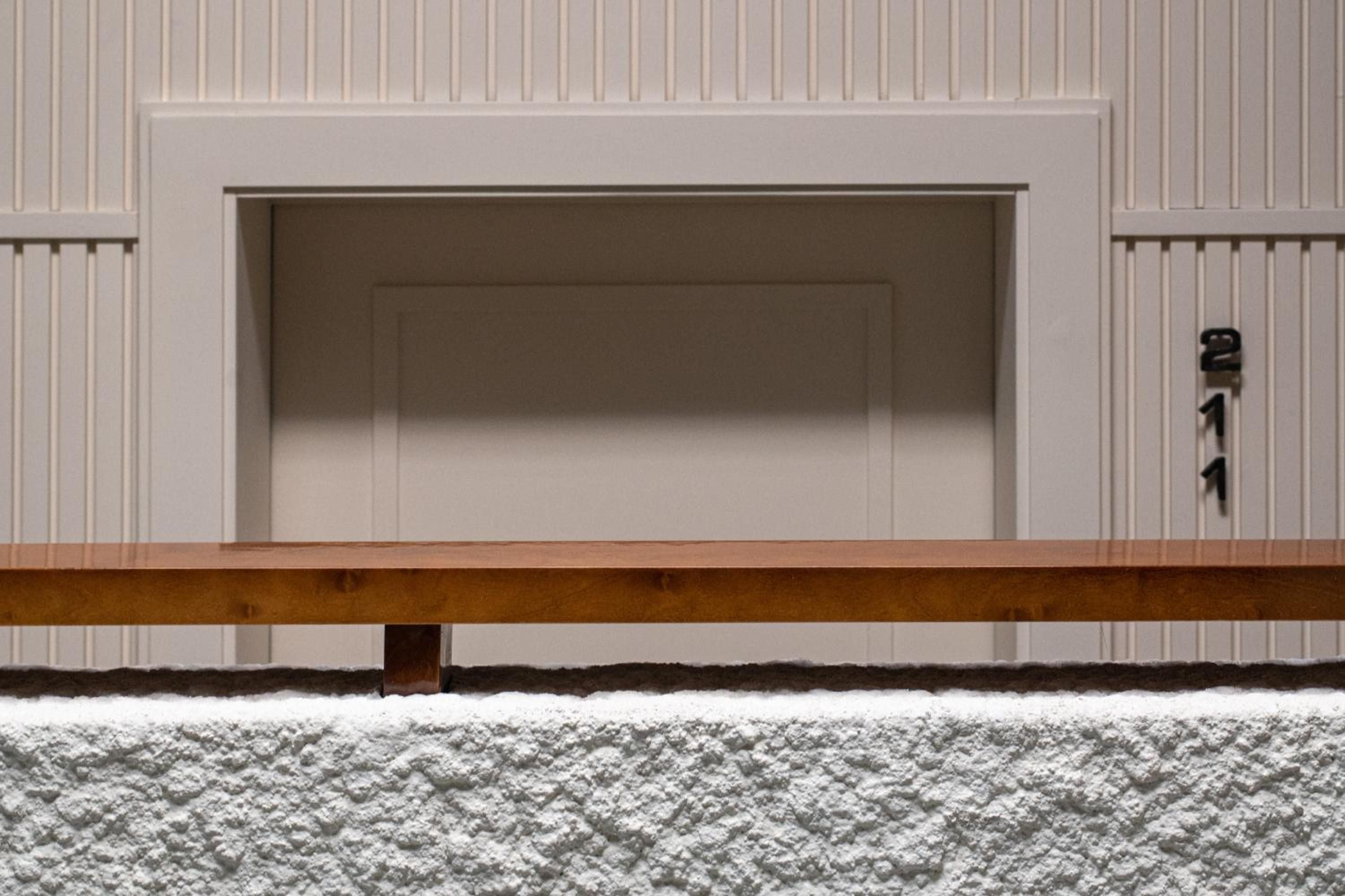 Clean architectural lines meet warm wood accents in this minimalist doorway detail, where textured white walls create subtle shadows and geometric precision.