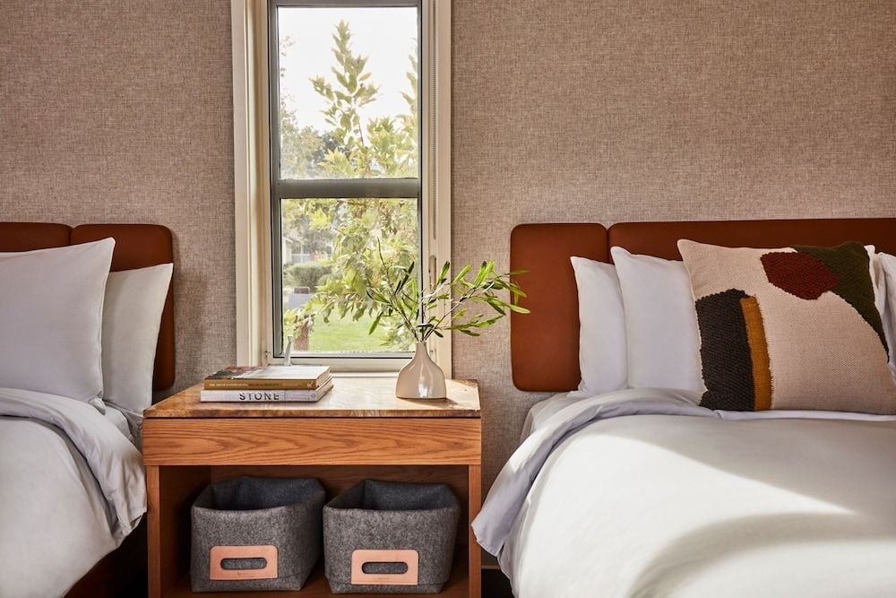 Warm wood nightstands and textured grasscloth wallpaper create an earthy sanctuary, where morning light streams through casement windows overlooking verdant Calistoga landscapes.