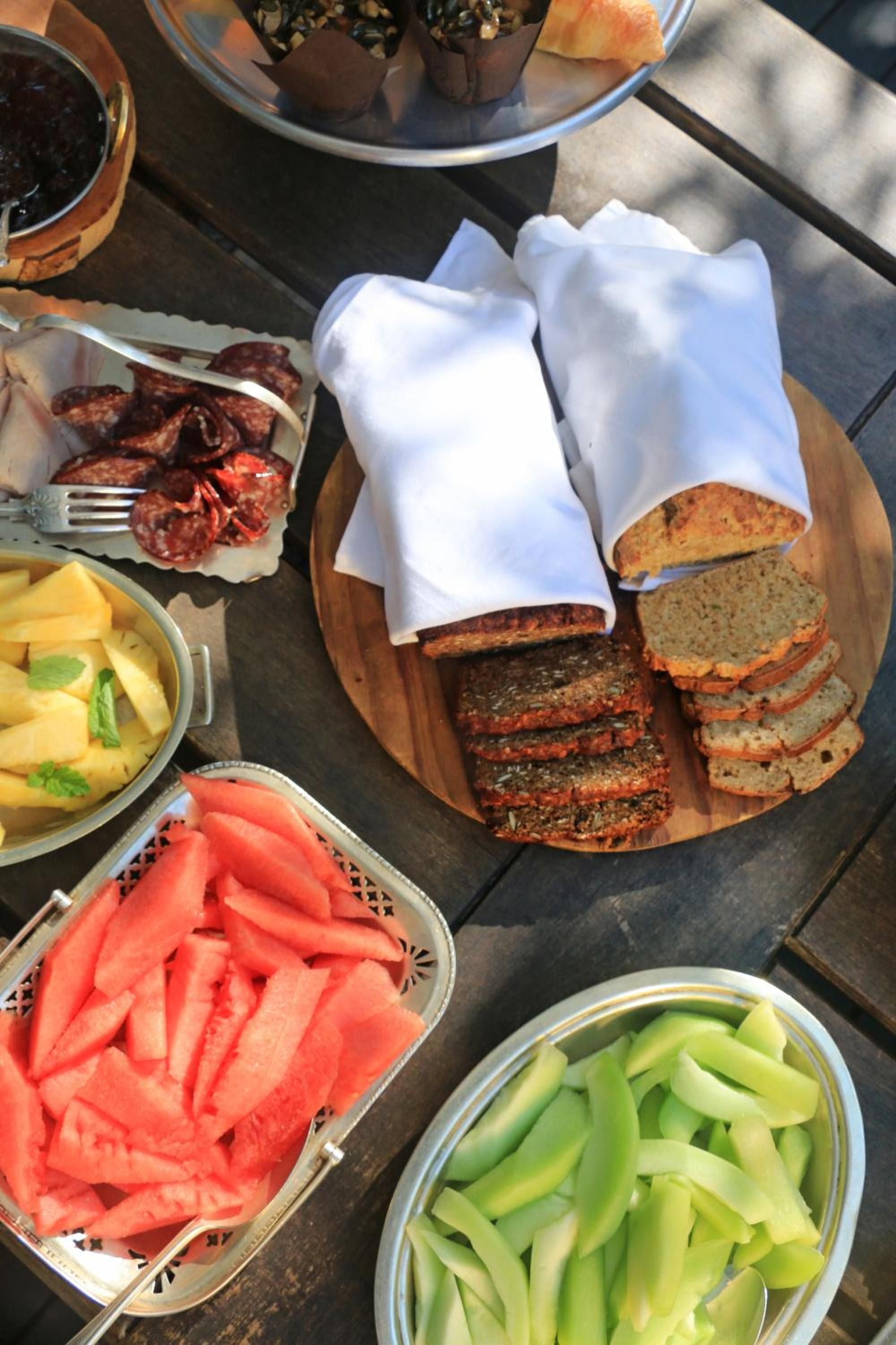 Artisanal breads wrapped in crisp white linens share the breakfast table with fresh watermelon and chorizo, creating an intimate riverside dining moment.