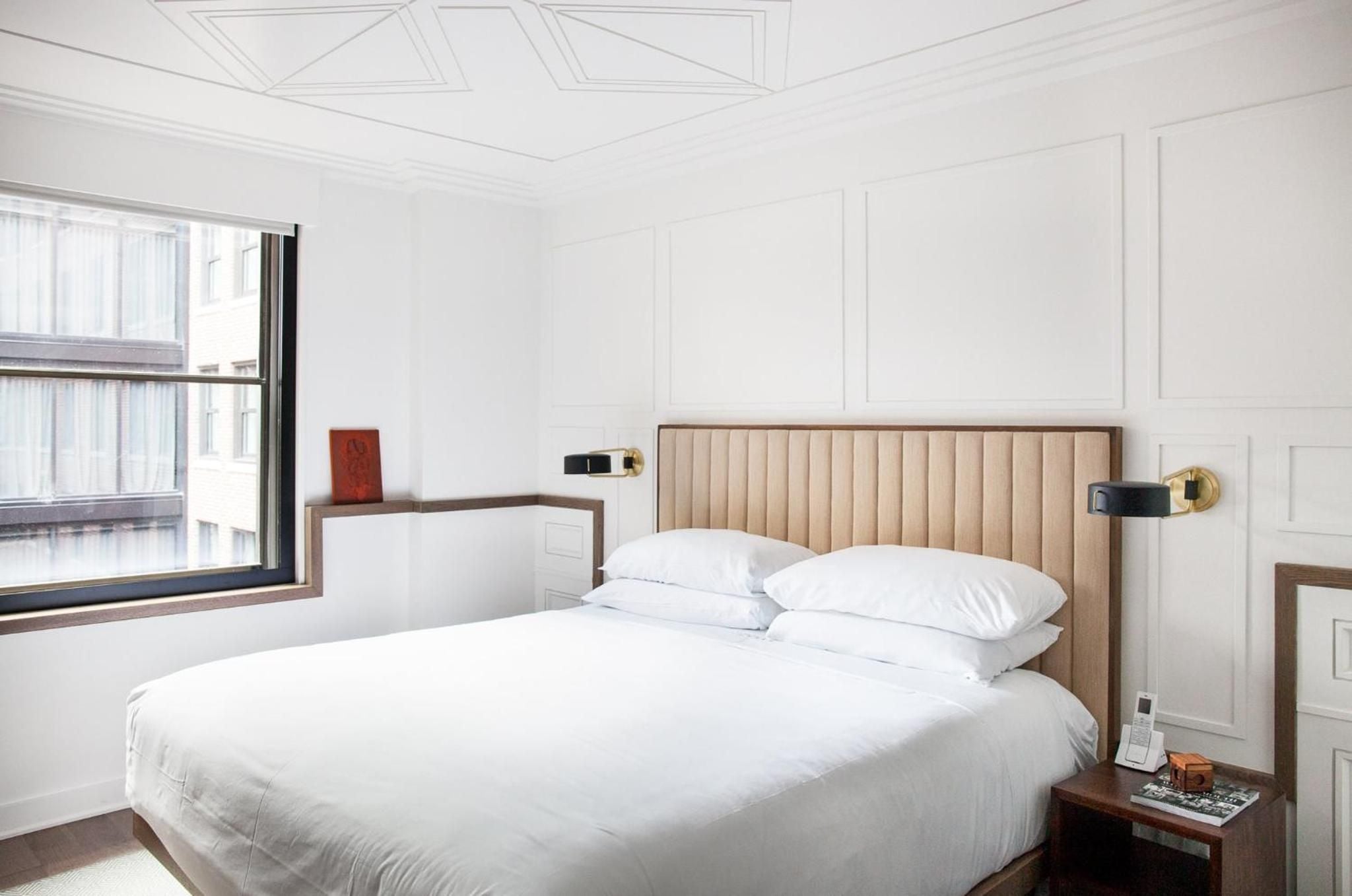 Channeled leather headboards and brass sconces create intimate reading nooks in guest rooms where geometric ceiling details cast subtle shadows across crisp white linens.