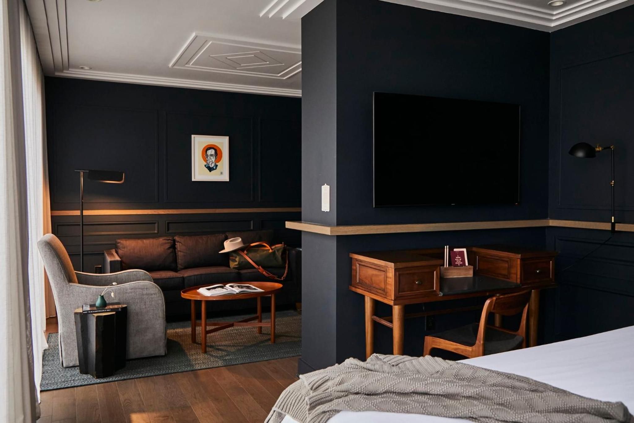 Navy walls create intimate cocoons around rich walnut furnishings, while geometric ceiling details and brass accents elevate this sophisticated guest room into a modern sanctuary.