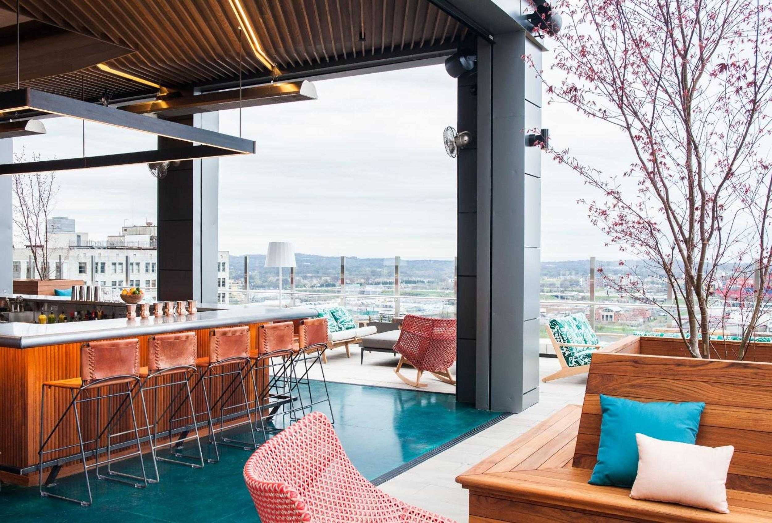 Copper bar stools gleam against turquoise waters while Nashville's skyline unfolds beyond this sophisticated rooftop retreat, where craft cocktails meet urban swimming.