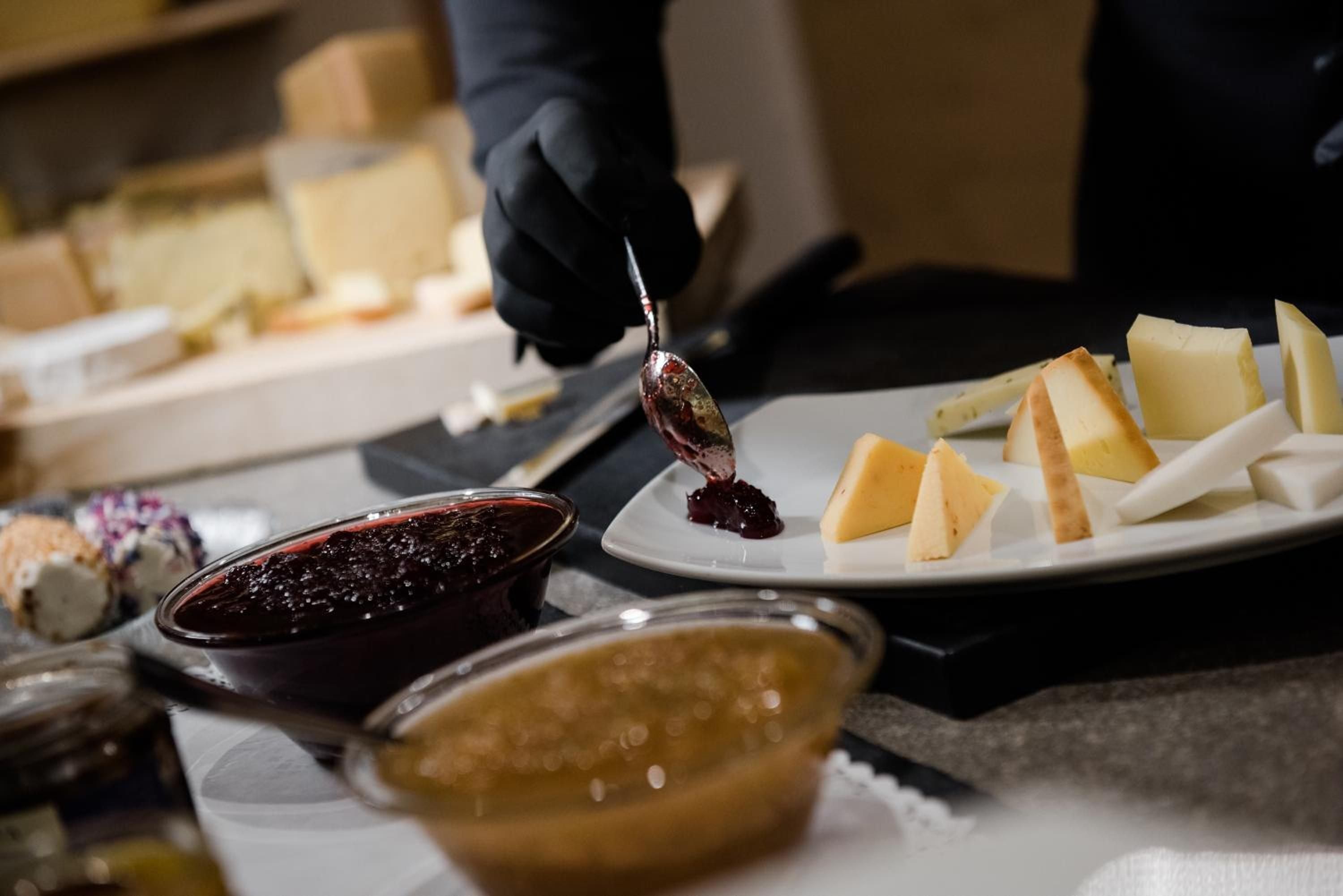 Gloved hands artfully plate local preserves alongside artisanal cheeses, transforming Alpine ingredients into an elegant culinary composition that celebrates regional terroir.