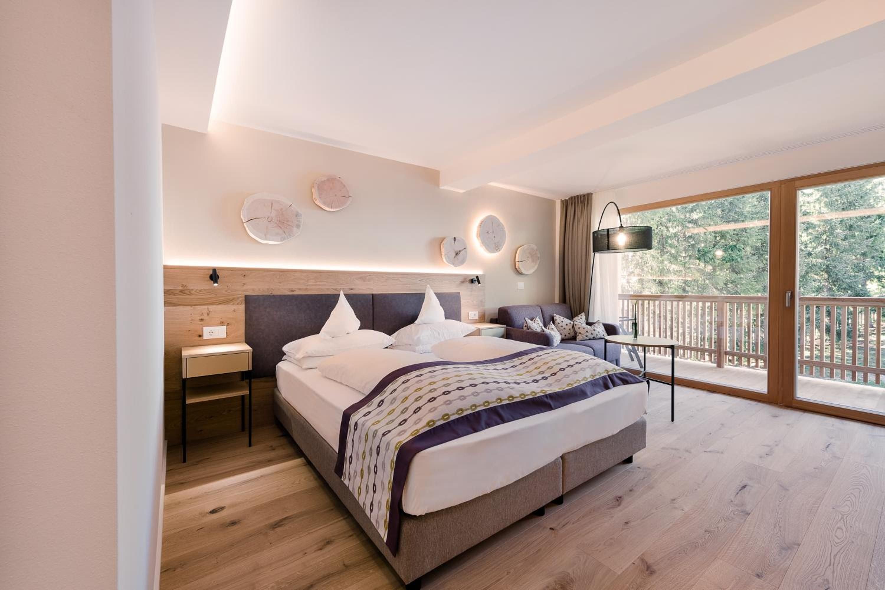 Alpine elegance meets modern comfort in this serene suite, where warm wood tones and circular wall art create intimacy against forest views through floor-to-ceiling windows.
