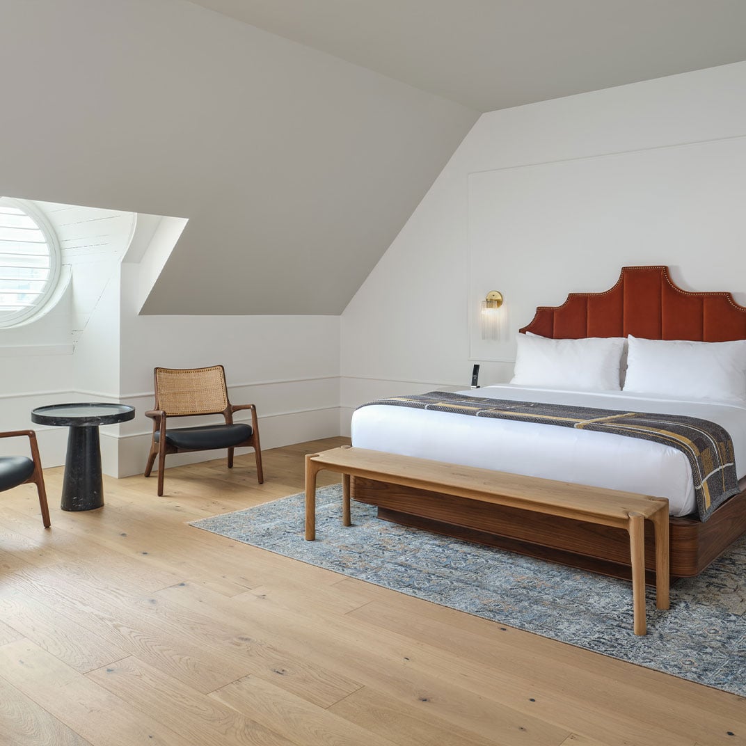 Slanted ceilings frame this attic suite where cognac leather headboards meet honey-toned wood floors, creating an intimate retreat beneath the eaves with Mid-Century modern charm.