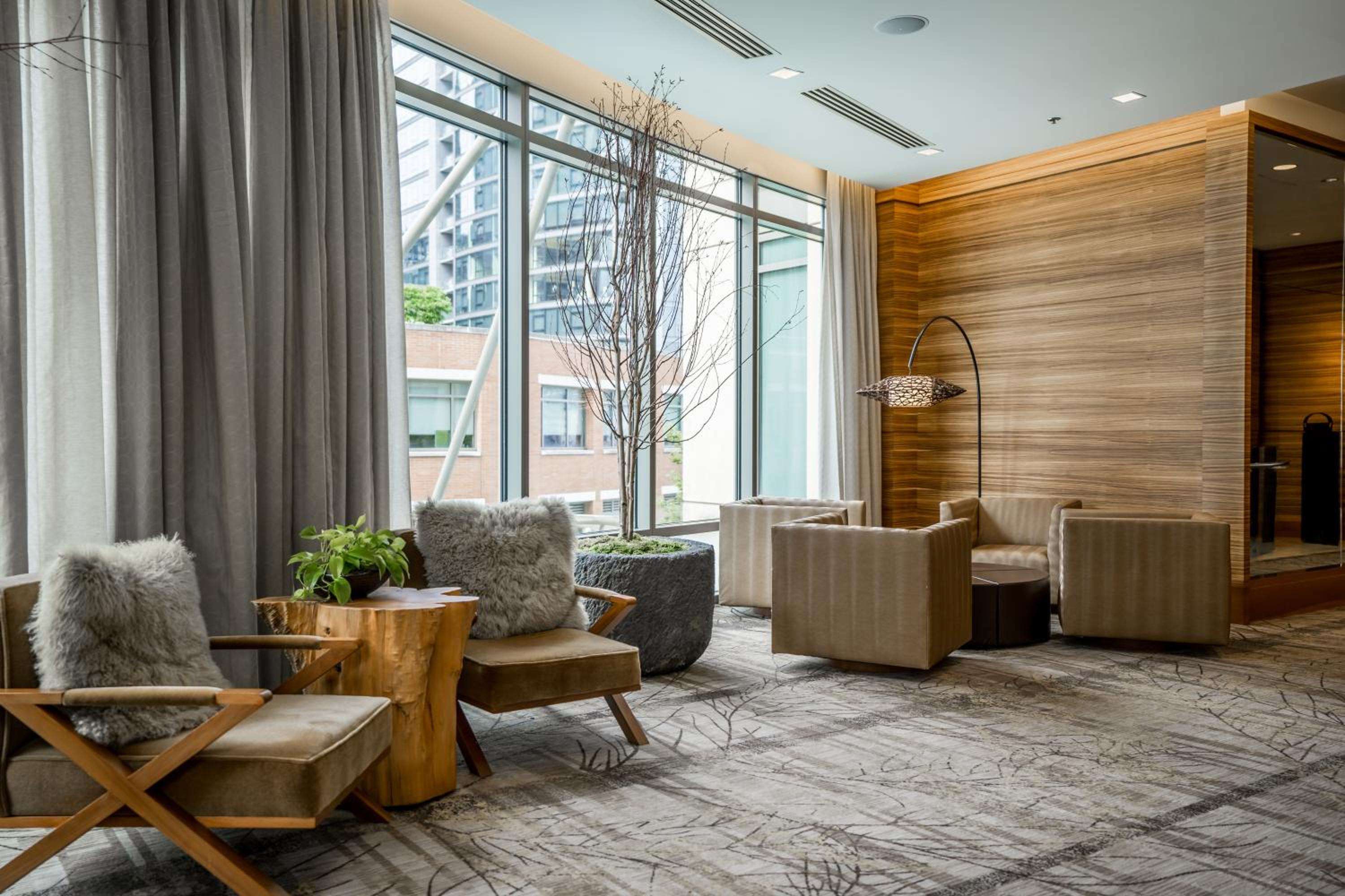 Natural wood paneling and plush seating create an inviting sanctuary where floor-to-ceiling windows frame Seattle's urban landscape through flowing curtains.