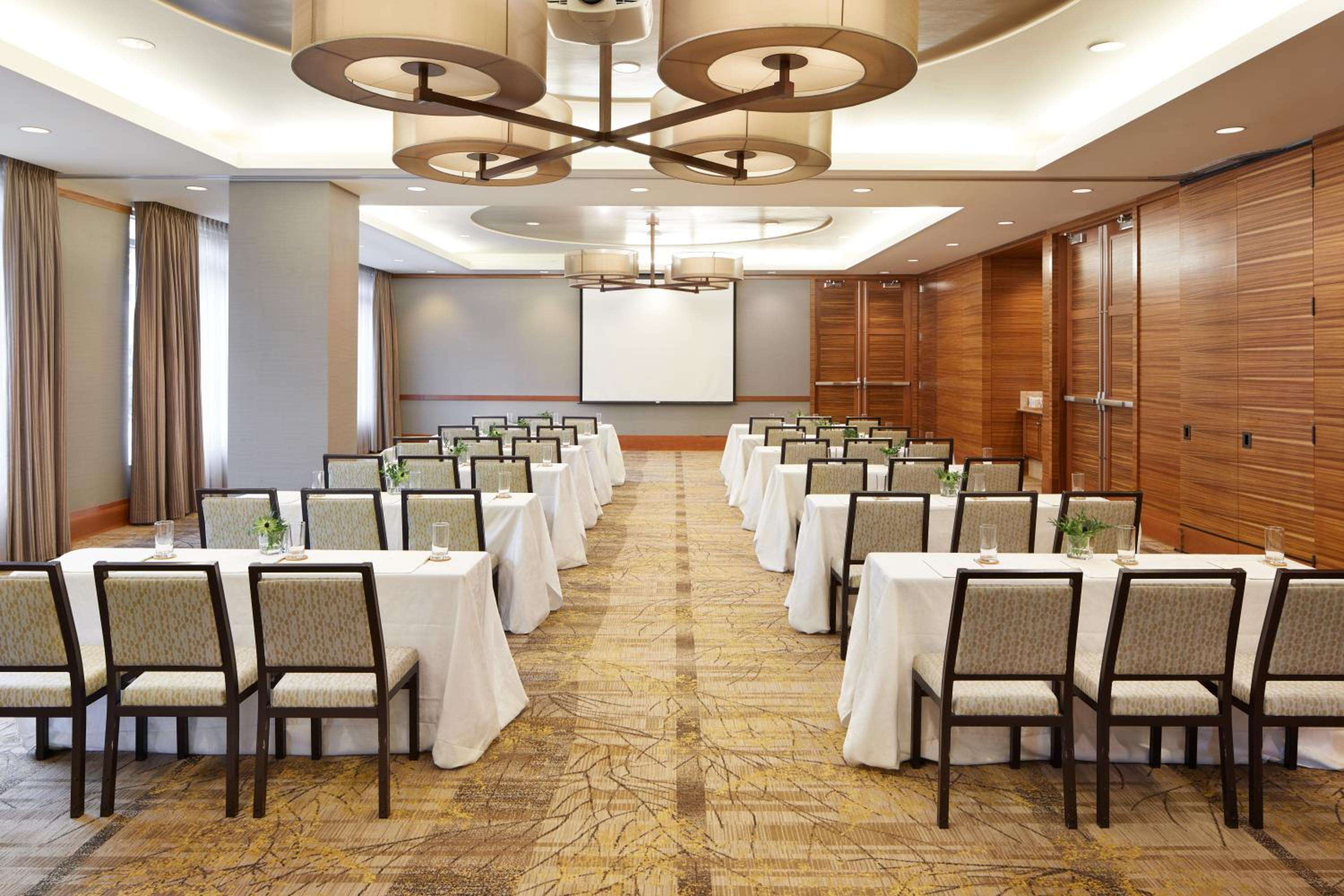 Warm wood paneling and contemporary chandeliers create an intimate boardroom atmosphere, where natural light filters through floor-to-ceiling windows onto polished tables.