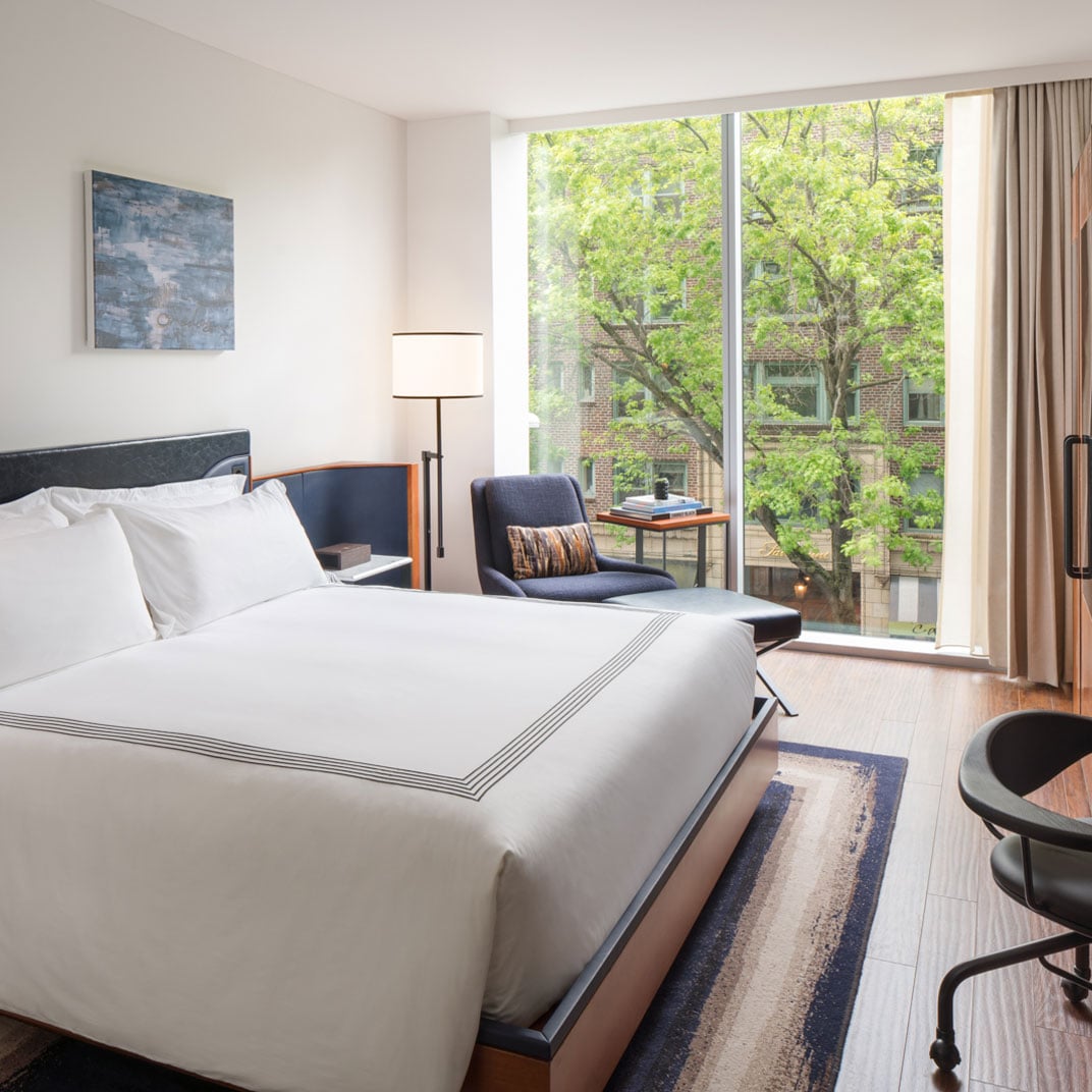 Floor-to-ceiling windows frame verdant Seattle streetscapes from this serene guest room, where navy accents and warm wood floors create a sophisticated urban retreat.