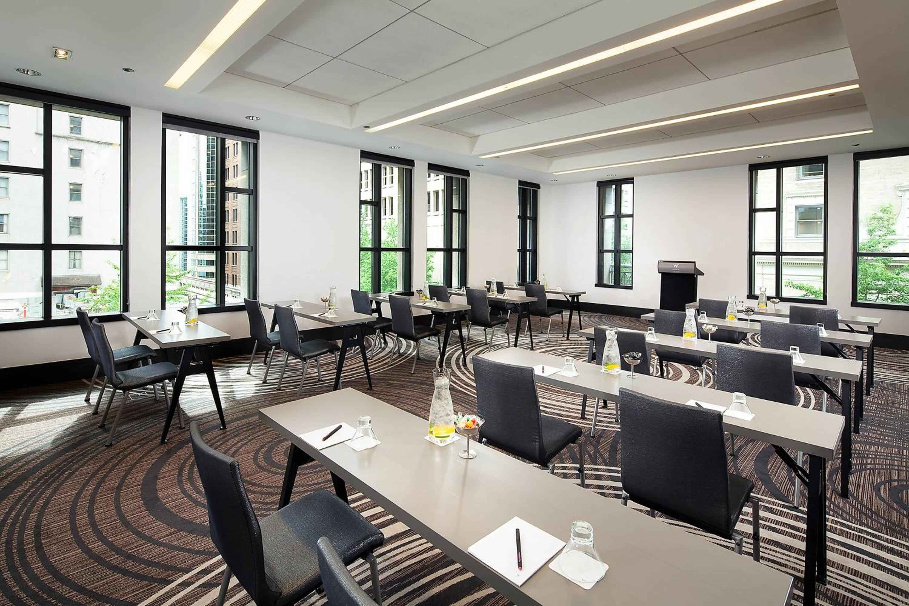 Floor-to-ceiling windows frame downtown Seattle while sleek tables await corporate gatherings in this naturally-lit boardroom, where geometric carpeting adds contemporary flair to strategic sessions.