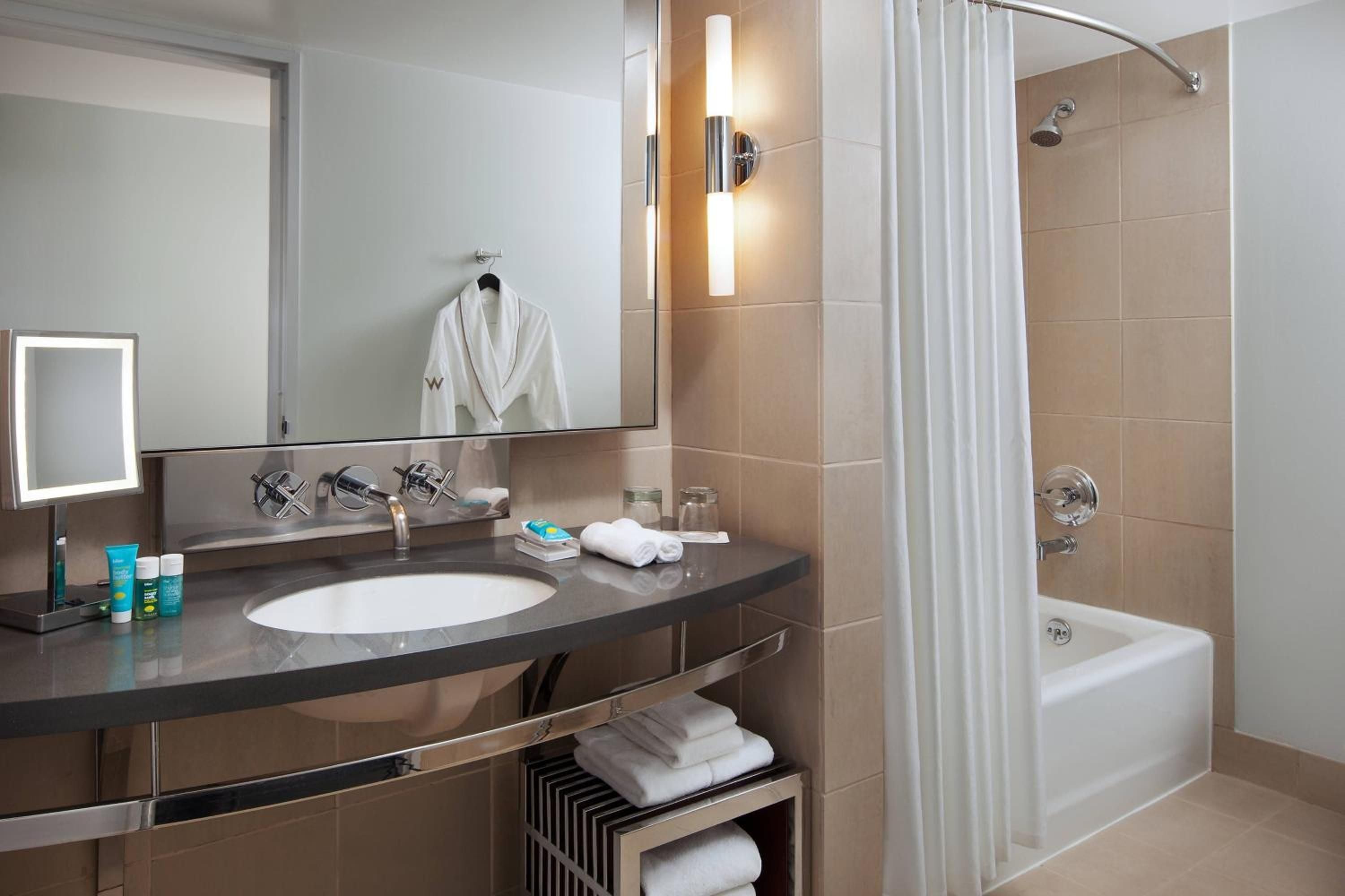 Sleek marble vanities and warm taupe tiles create a spa-like sanctuary, where polished chrome fixtures gleam under soft sconce lighting in this contemporary retreat.