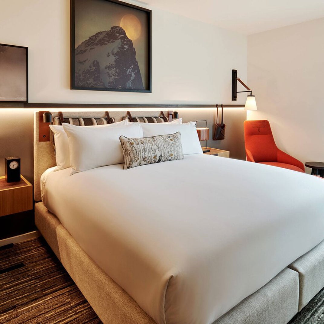 Warm wood tones and soft lighting create an inviting refuge, while mountain photography and thoughtful touches like the vibrant orange chair add sophisticated alpine character.