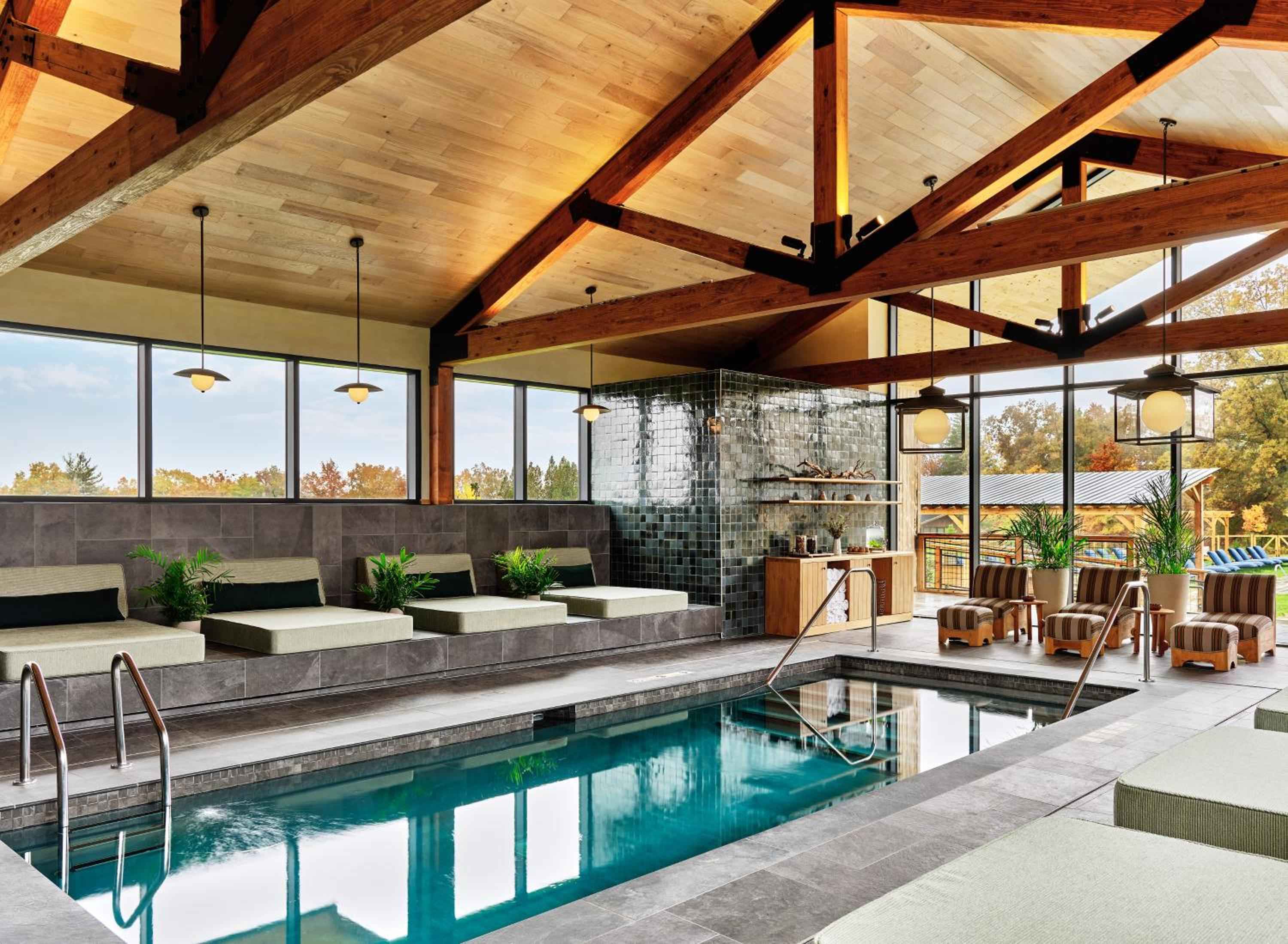 Exposed timber beams frame an infinity-edge lap pool where floor-to-ceiling windows blur boundaries between the serene spa sanctuary and autumn countryside beyond.